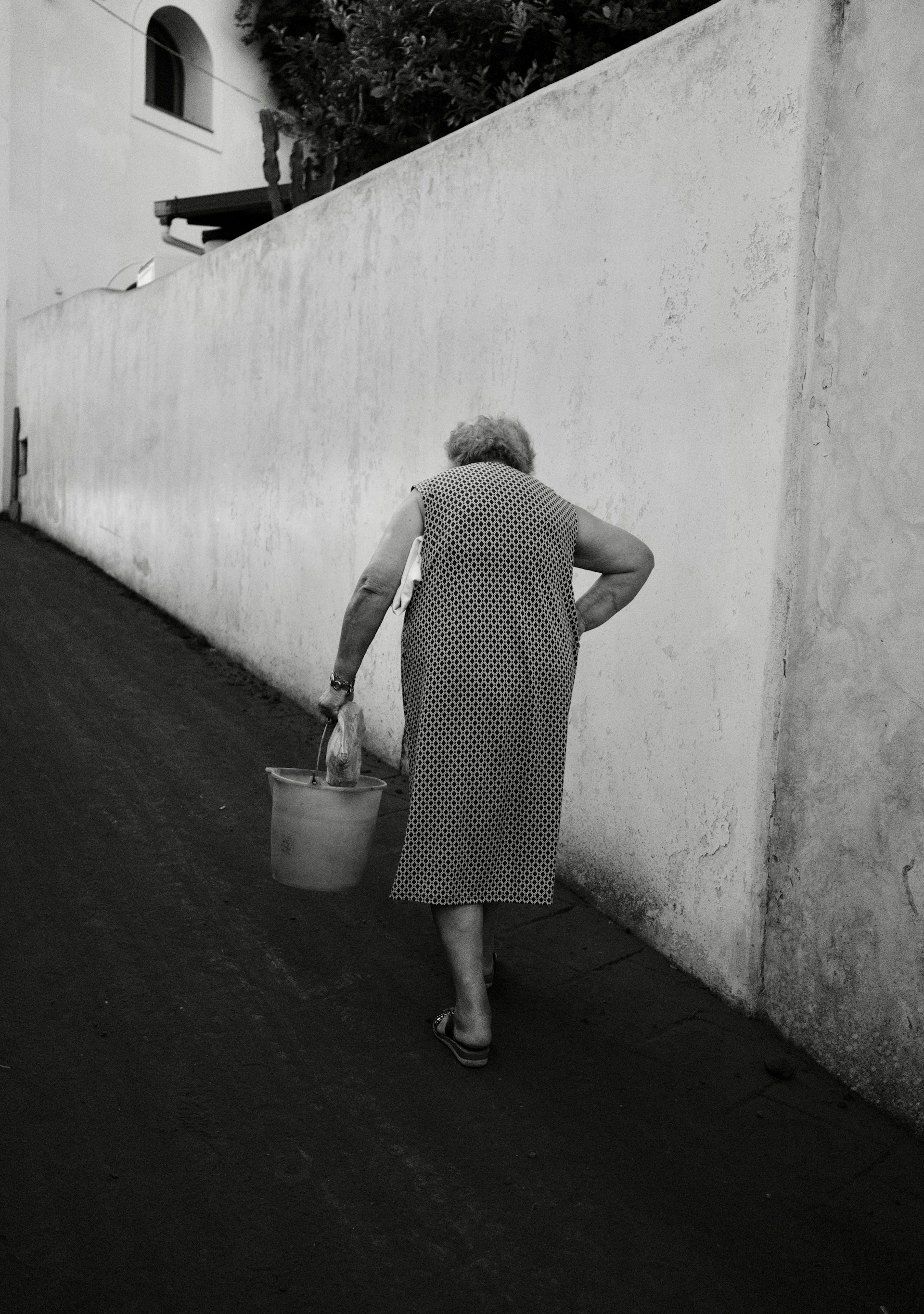 Grayscale shot of an older woman walking with a bucket | Source: Unsplash