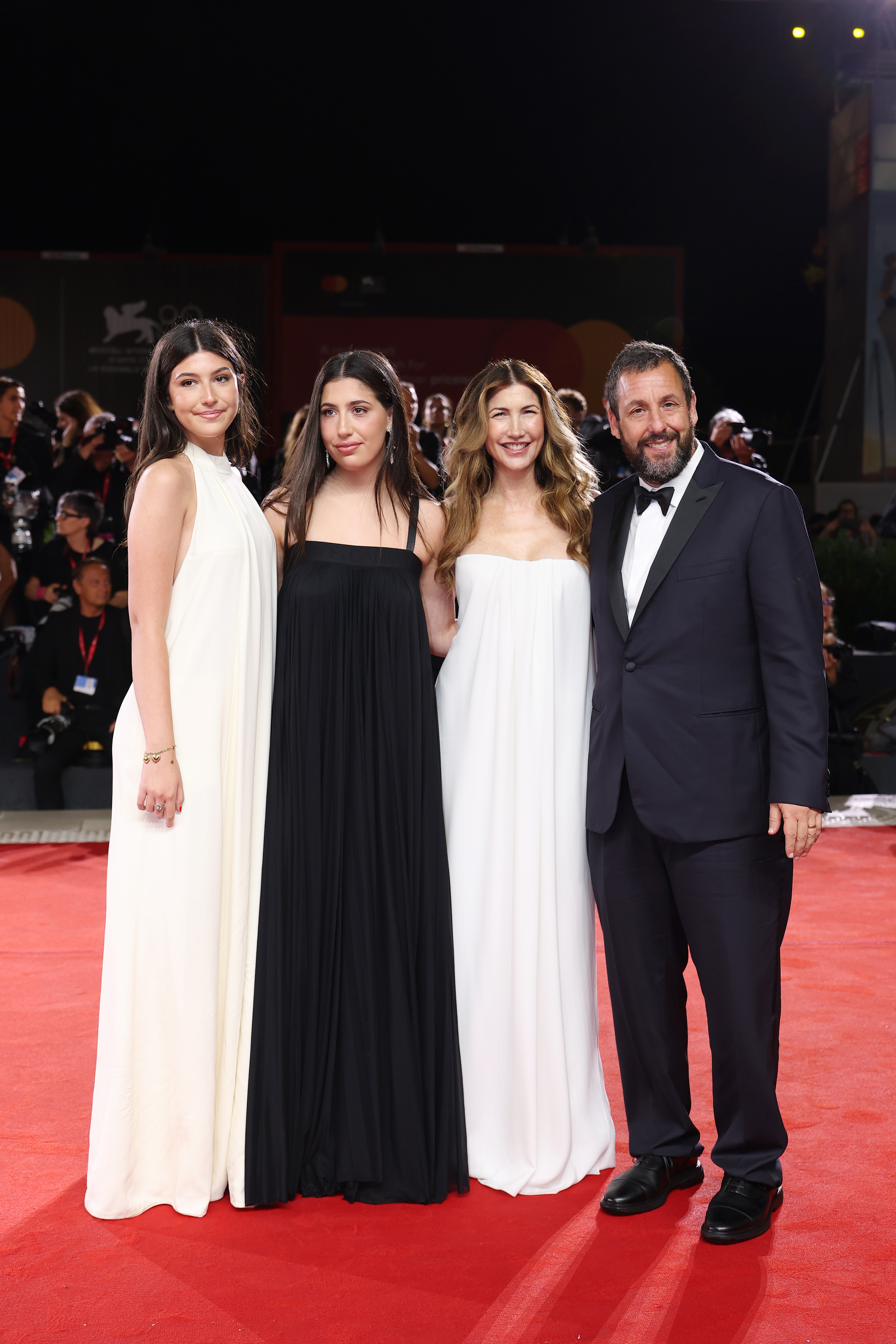 A full shot highlights the stunning dresses of Sunny, Sadie, and Jackie Sandler, while Adam looks handsome in a sleek suit, a change from his casual style. Adam and Jackie beam with joy, while their daughters wear calm, contented expressions. The family are a picture of elegance and harmony as they grace the red carpet.