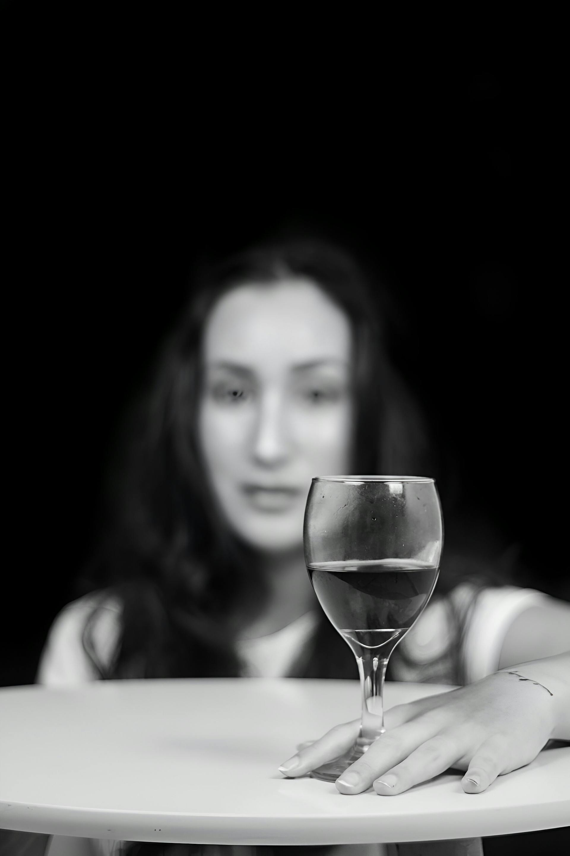 Grayscale of a woman sitting at a table with a glass of wine | Source: Pexels