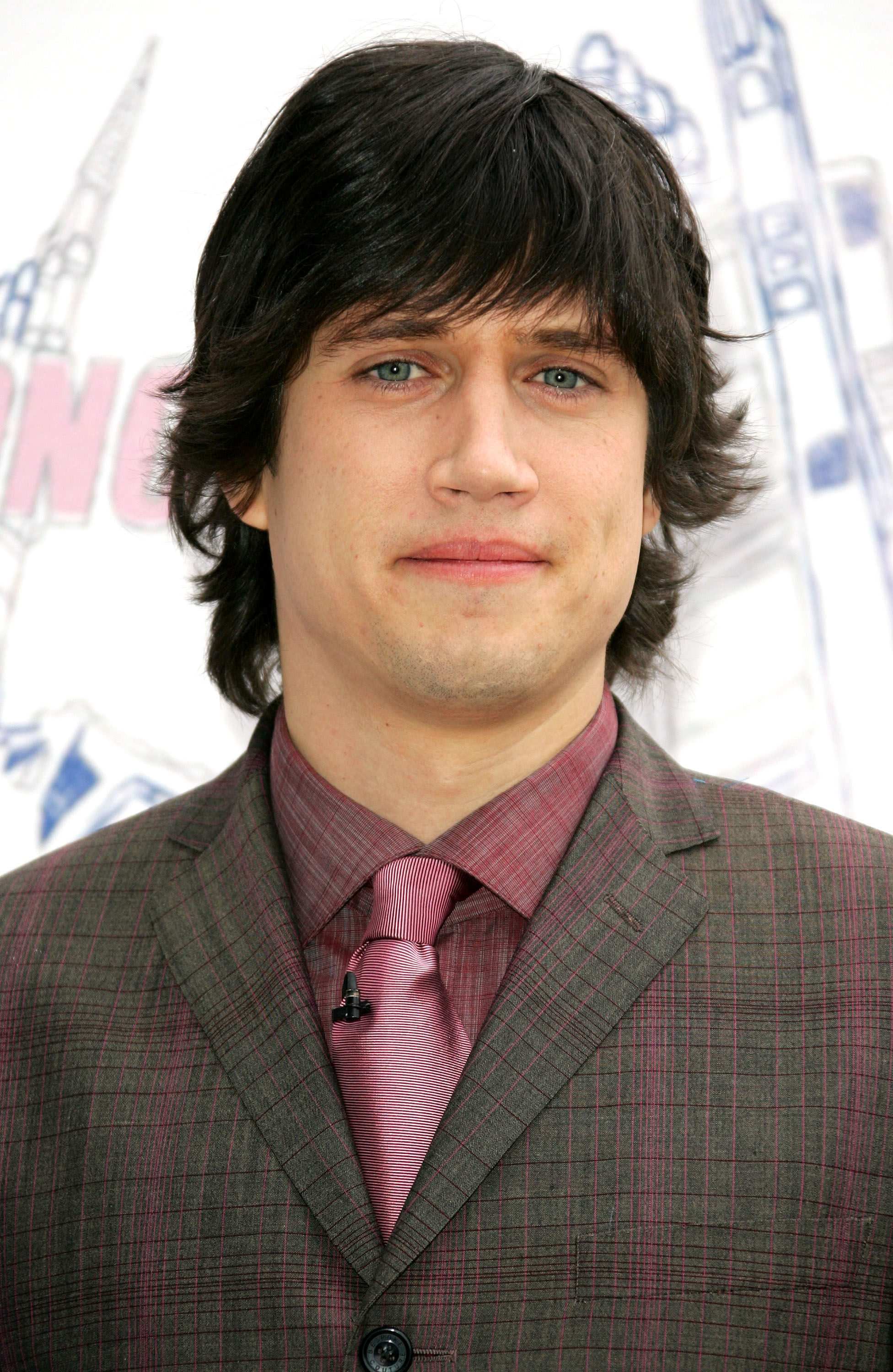 The TV and radio presenter appears in a checked suit paired with a matching shirt and tie, holding a composed expression as he faces the camera.