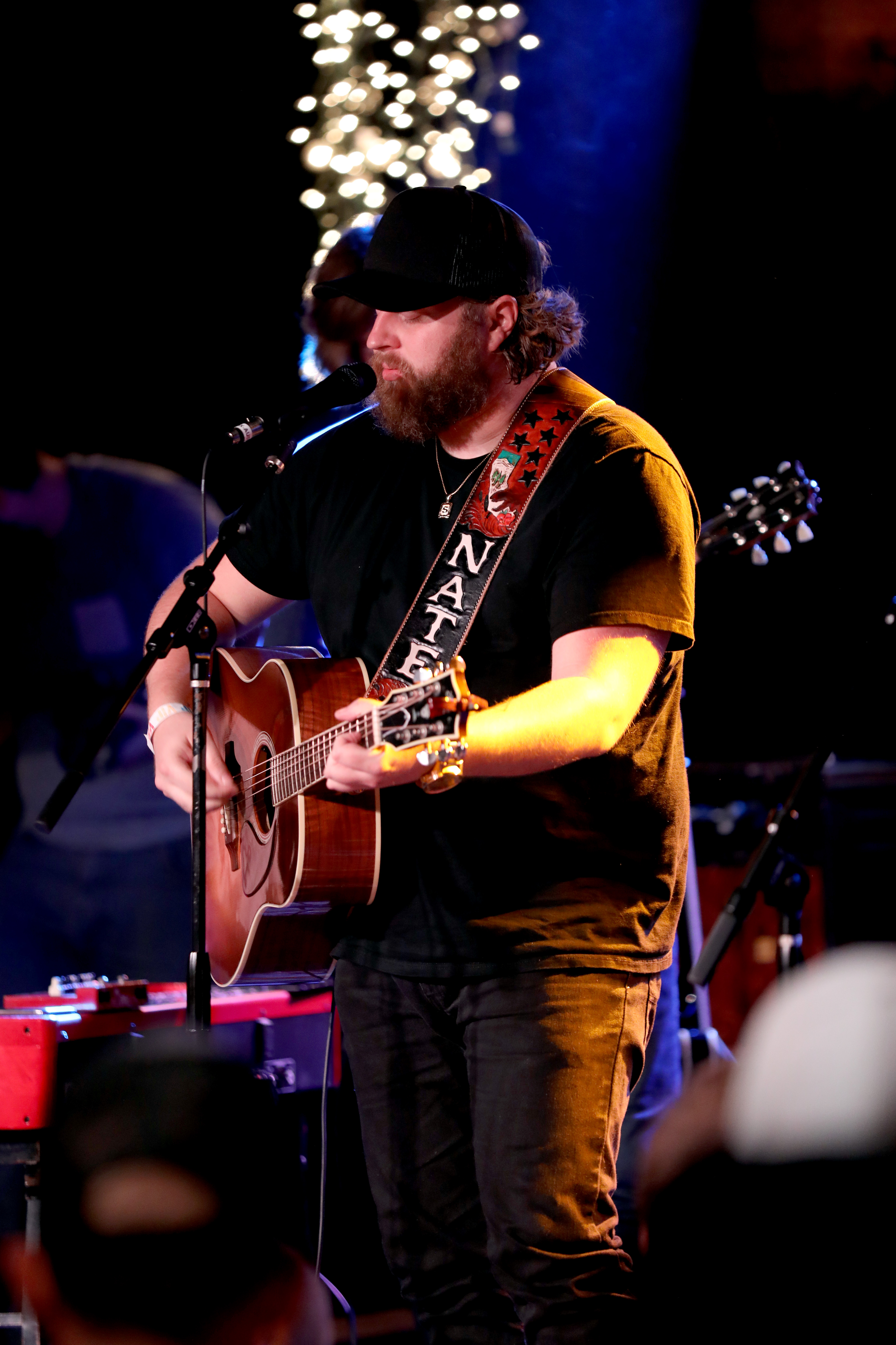 Nate Smith leans into the microphone with his acoustic guitar in hand, bringing a focused intensity to the intimate stage as warm lights glow behind him.