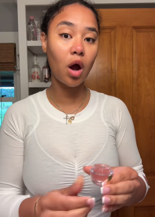 Brianna McKnight stands in a bathroom holding a lip gloss bottle, from a post dated August 30, 2025. | Source: TikTok/brimcknighttt