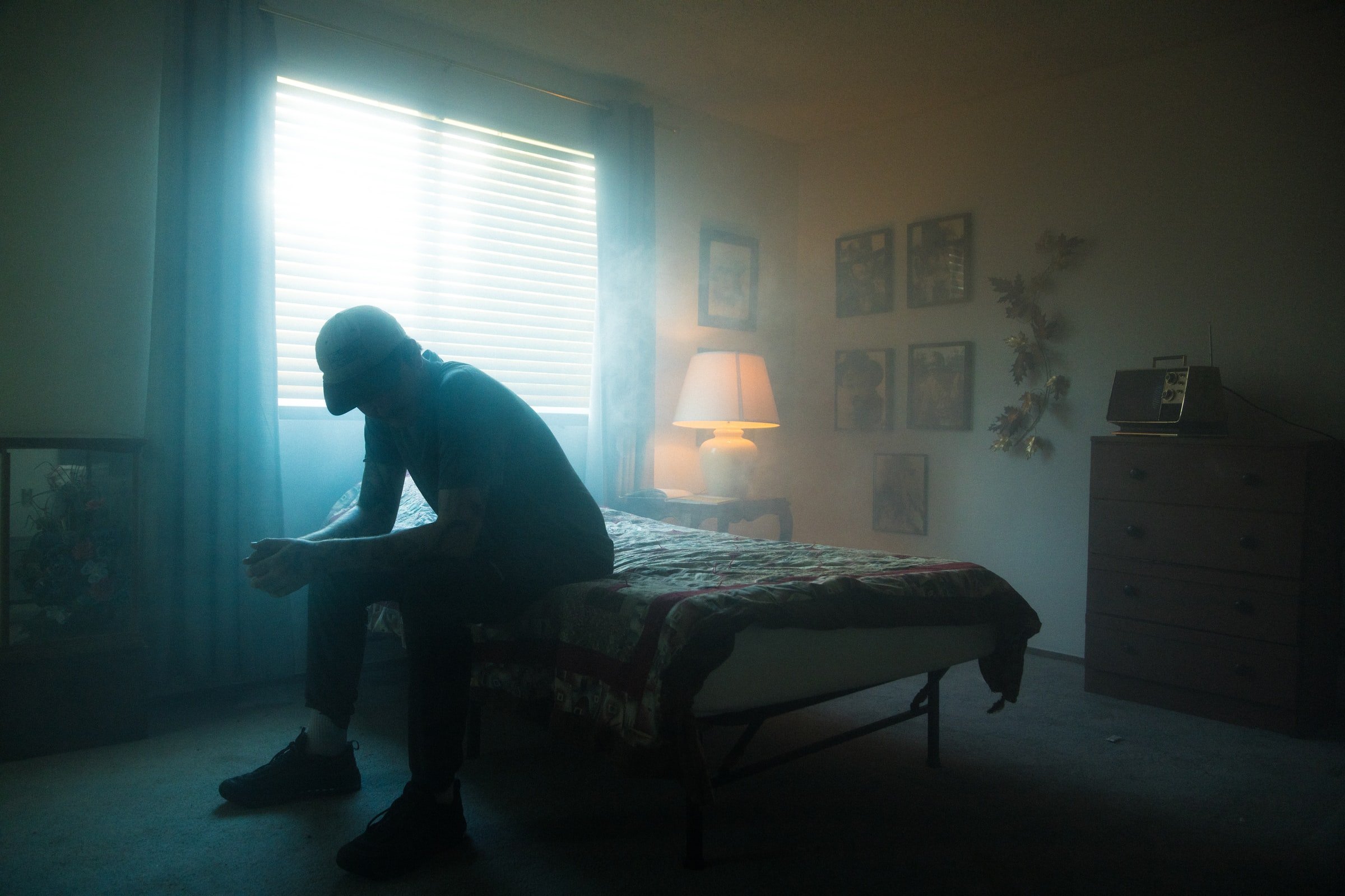 A man sitting on a bed in a dark room. | Source: Unsplash
