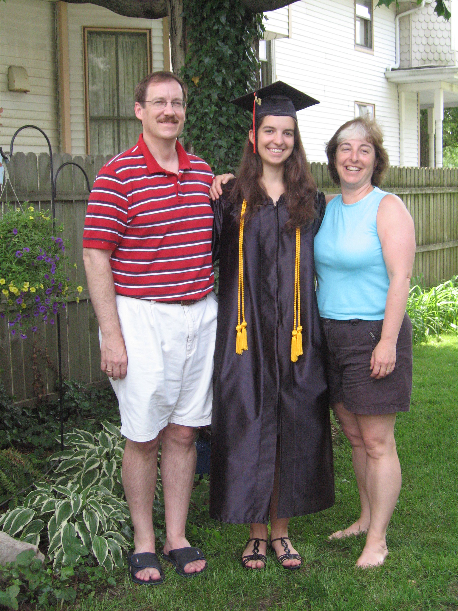 A woman wearing a graduation gown and cap while standing next to her parents | Source: flickr.com