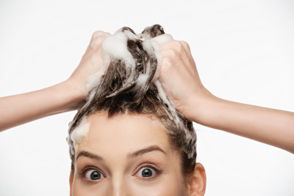 Mujer sorprendida lavándose el pelo con champú. | Foto: Shutterstock