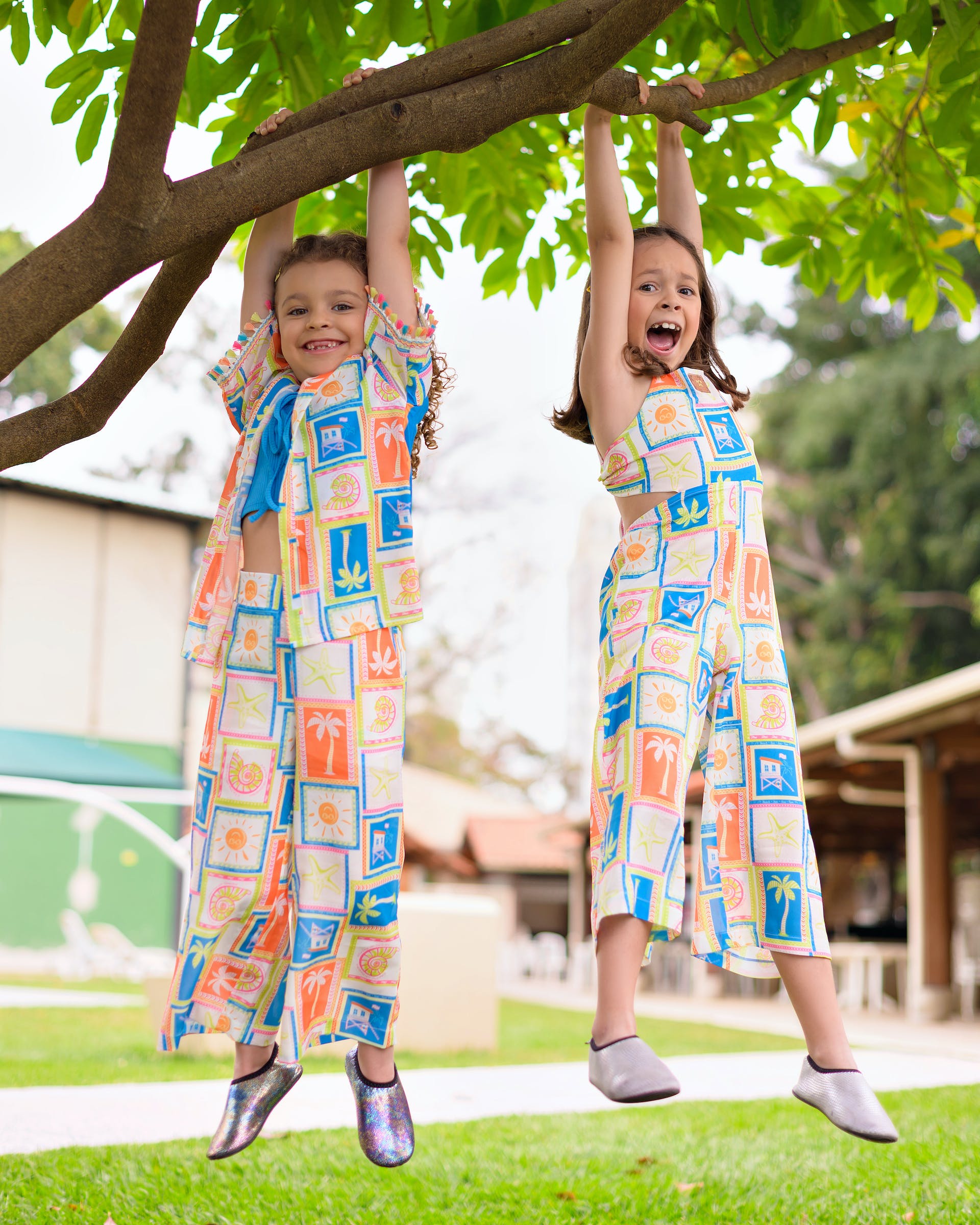 Two smiling young girls wearing the same dress are hanging from a tree branch | Source: Pexels