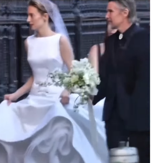 Maya Hawke walks in her white gown and veil, lifting her skirt as her father, Ethan Hawke, follows closely beside her, carrying a cascading white bouquet. | Source: Instagram/relationships.usa