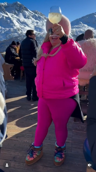 Gemma Collins raises a drink toward the camera while dancing in the sunshine, continuing her playful moment on the slopes in St Moritz. | Source: Instagram/gemmacollins