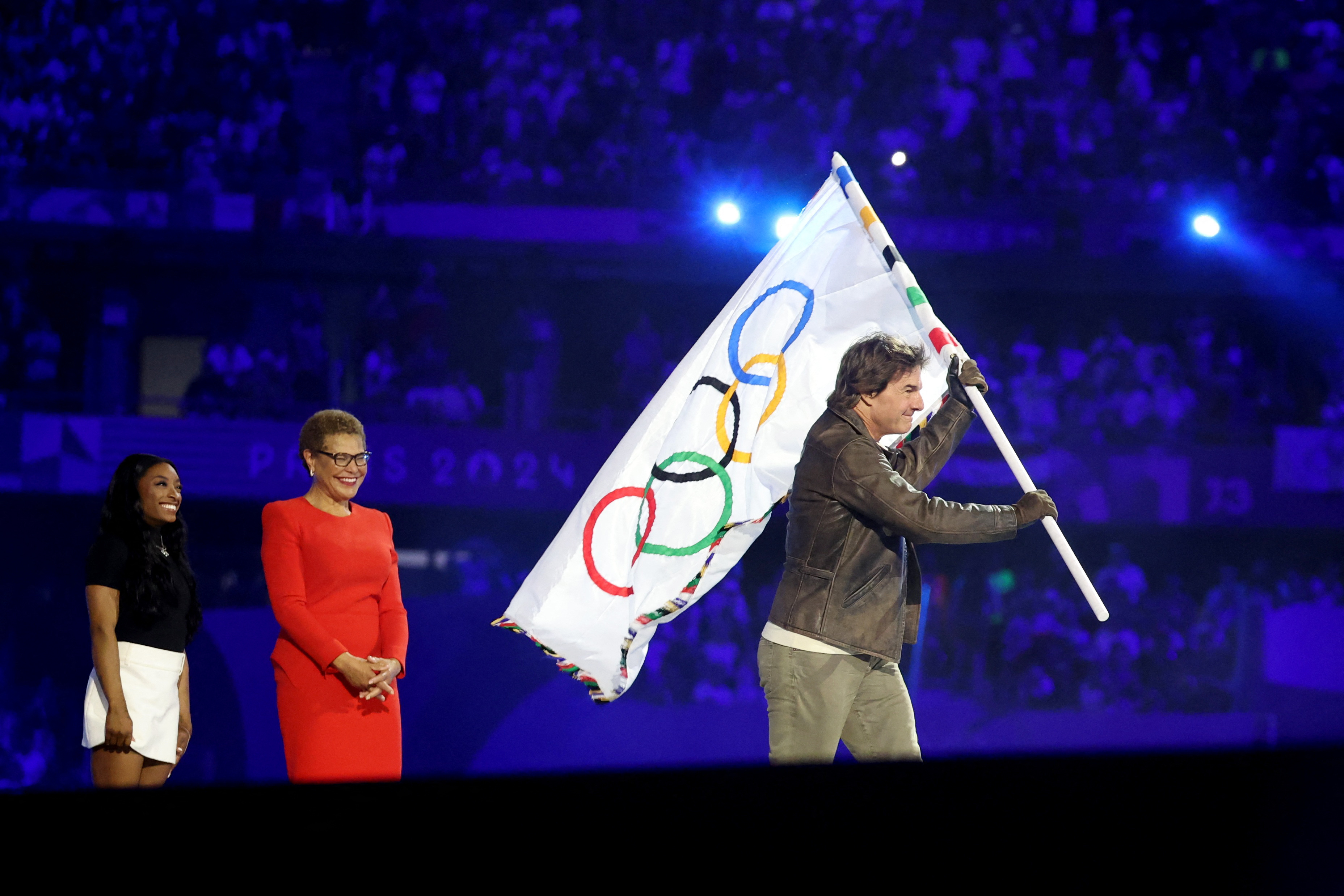 Mayor Karen Bass and Simone Biles looking on as Tom Cruise holds the Olympic flag during the closing ceremony of the Olympic Games in Paris on August 11, 2024 | Source: Getty Images