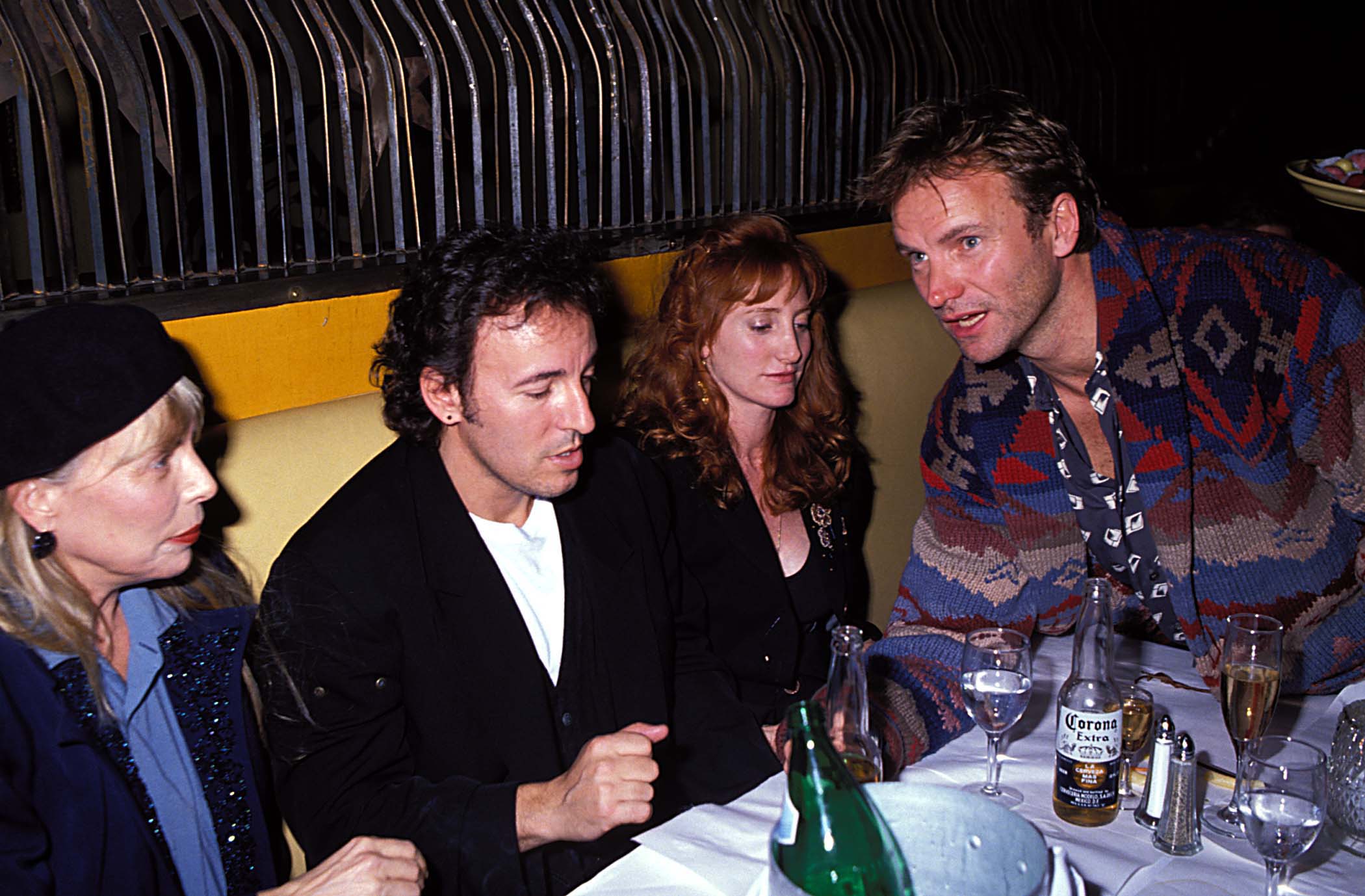 In this intimate backstage photo from a 1991 post-concert party, Sting is seated alongside Joni Mitchell, Bruce Springsteen, and Patti Scialfa. The group appears relaxed and deep in conversation, offering a rare glimpse into the offstage camaraderie of some of music’s most influential artists.