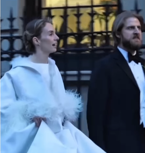 Wrapped in a white coat with feathered cuffs, Maya Hawke walks beside Christian Hutson in a classic black tuxedo. | Source: Instagram/relationships.usa