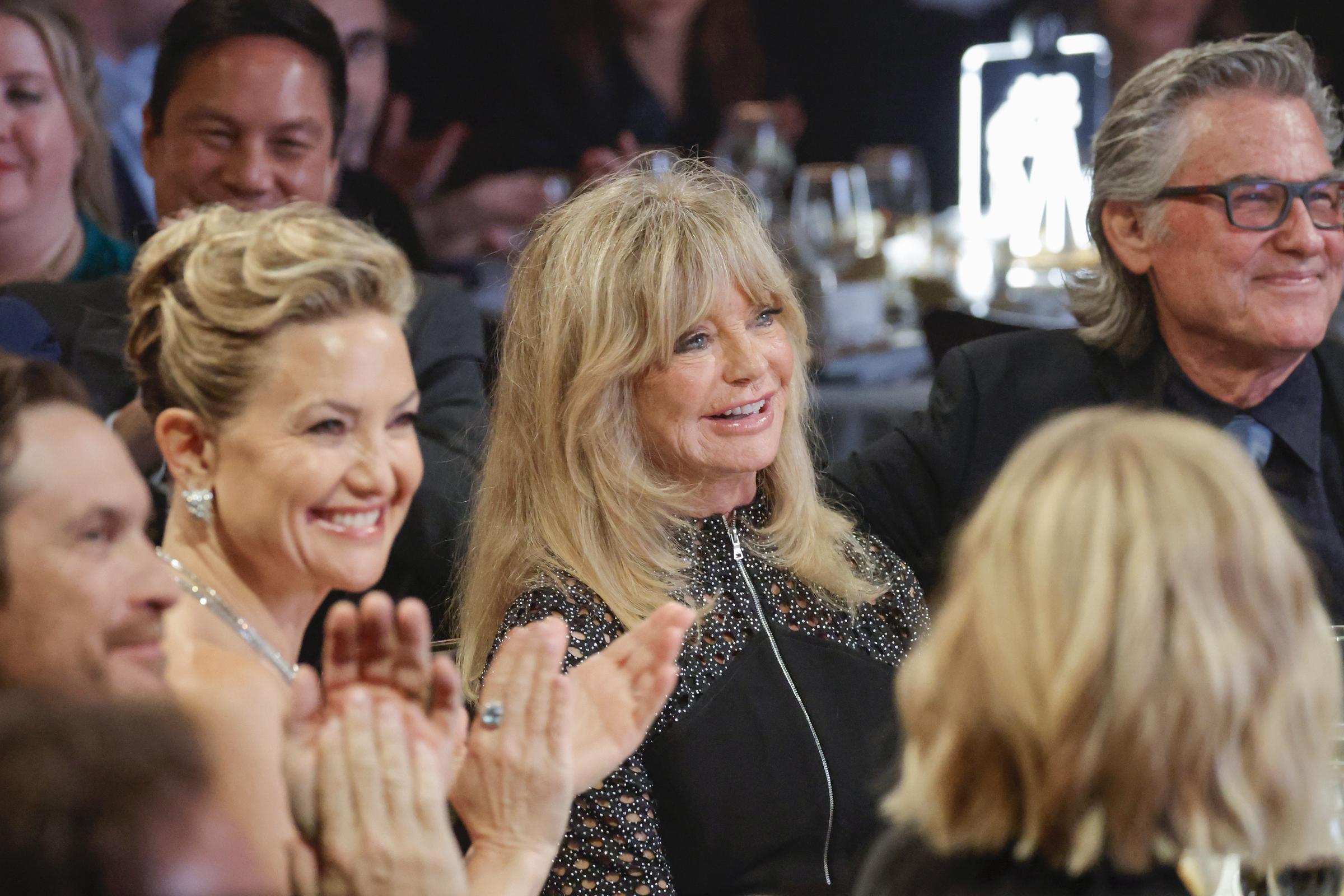 Kate Hudson, Goldie Hawn, and Kurt Russell all smiling as they sit at their dinner table at the glamorous event. | Source: Getty Images
