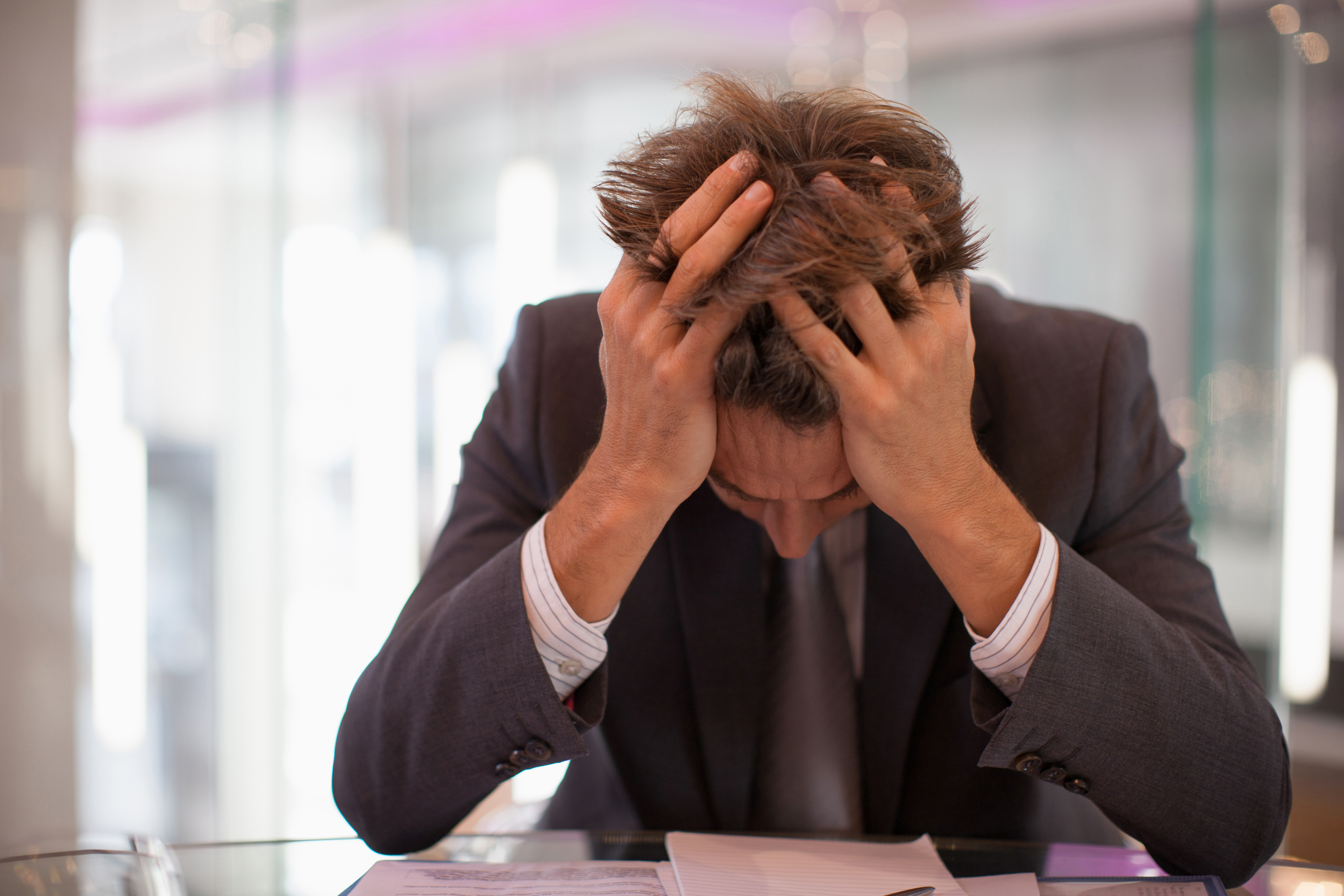 Frustrated businessman sitting at desk with head in hands | Source: Getty Images
