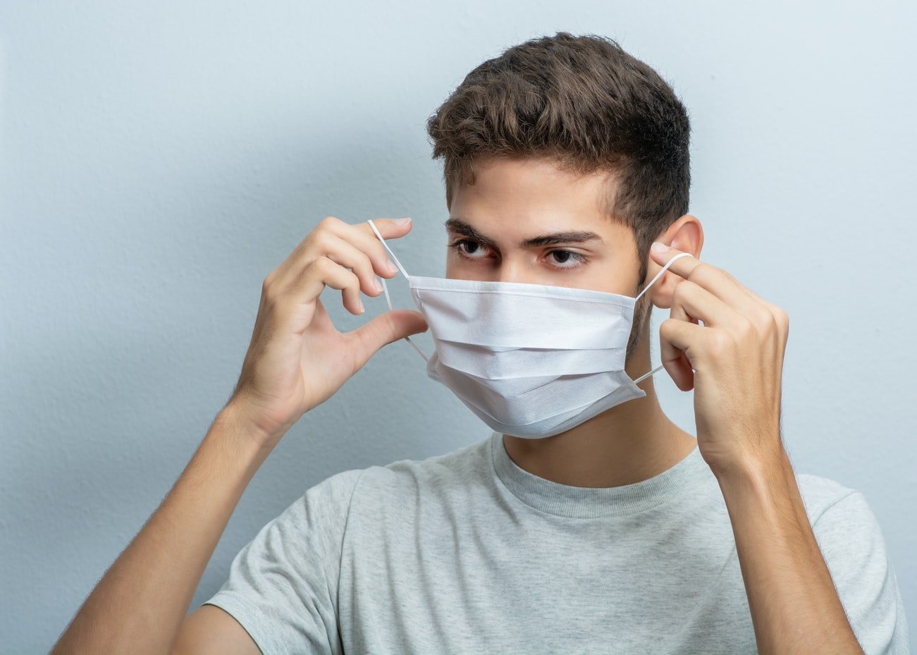 Un jeune homme mettant son masque. l Source : Unsplash