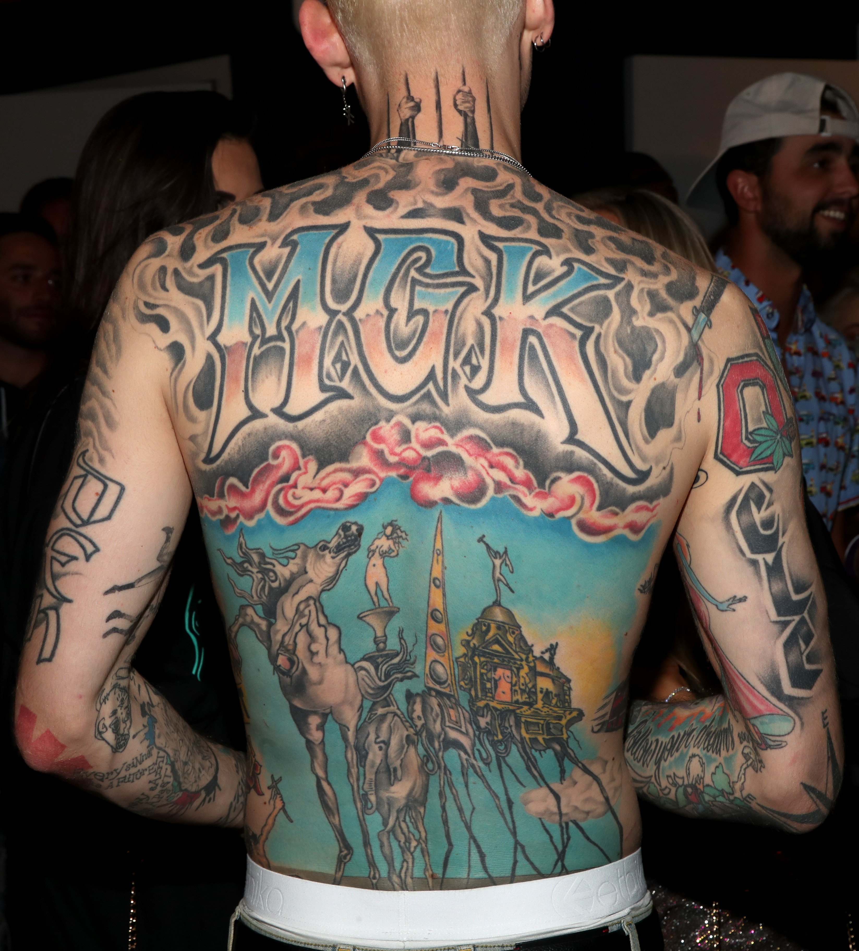 Machine Gun Kelly's "MGK" and Salvador Dali tattoo fully covering the back of his torso while "DEN" and "CLE" tattooed on the back of his arms. | Source: Getty Images