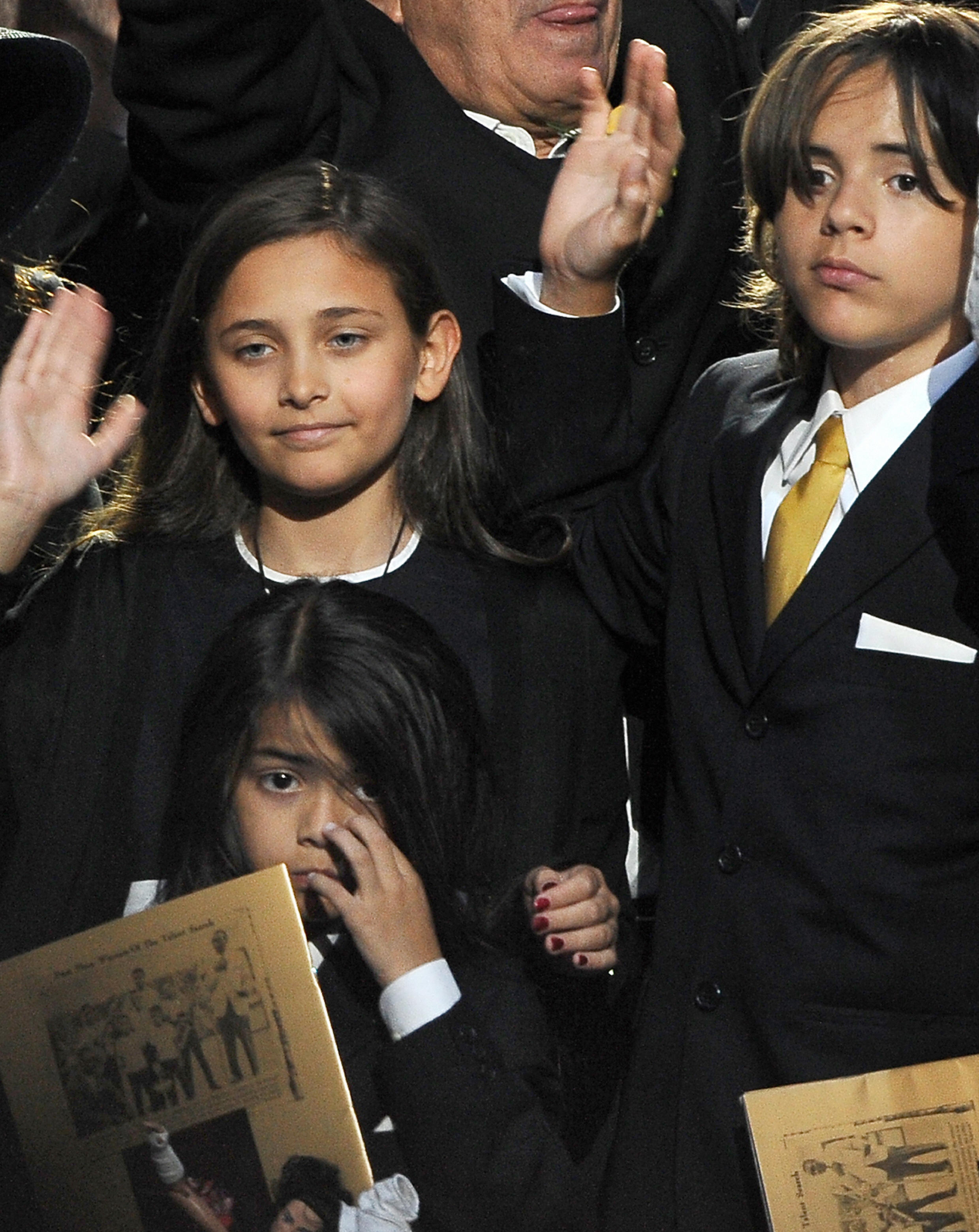 A young Paris Jackson (left) stands beside her brothers, Prince Michael Jackson II — known as Blanket — and Prince Michael Jackson I (right), as they wave to the crowd at their father Michael Jackson’s memorial service at the Staples Center in Los Angeles on July 7, 2009. The moment marked one of Paris’s earliest public appearances, capturing a poignant chapter in the Jackson family’s story.