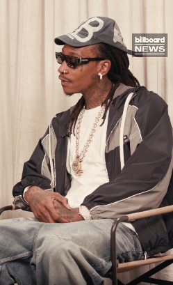 Wiz Khalifa wears a cap, sunglasses, and a layered outfit while seated in a post dated May 12, 2025. | Source: Facebook/Cain's Ballroom