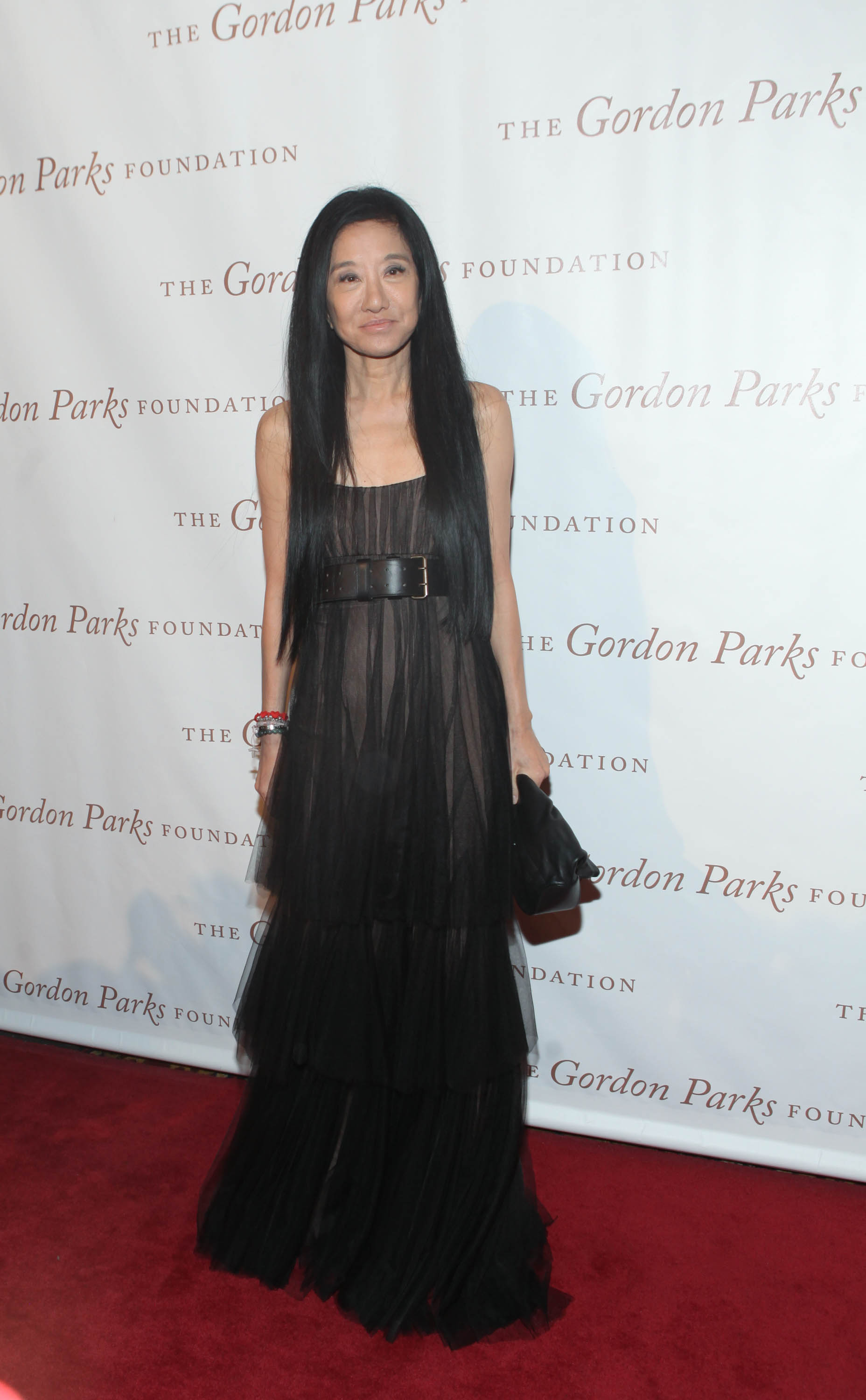 Vera Wang wears a sheer black belted gown to the Gordon Parks Foundation awards dinner. With minimal accessories and a small clutch in hand, she poses in front of the step-and-repeat, maintaining her signature understated, yet fashion-forward style.