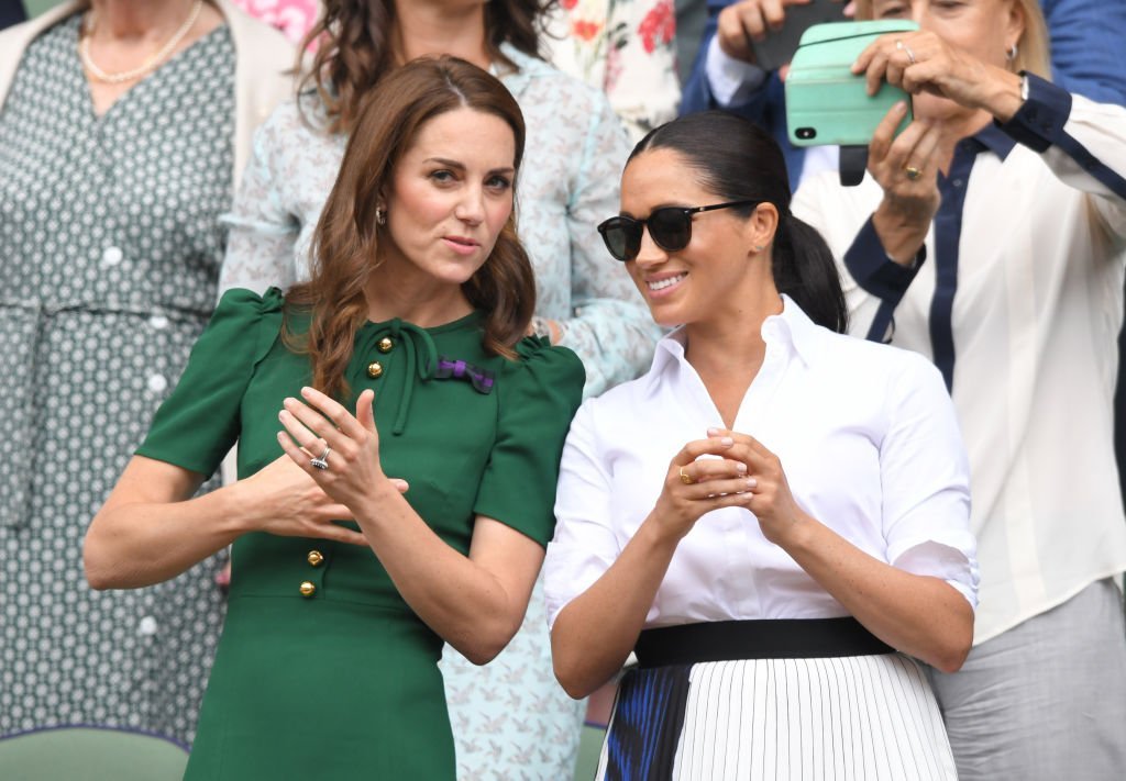 Kate Middleton and Meghan Markle chat while standing in the Royal Box on Centre Court during the Wimbledon Tennis Championships on July 13, 2019, in London, England | Source: Karwai Tang/Getty Images