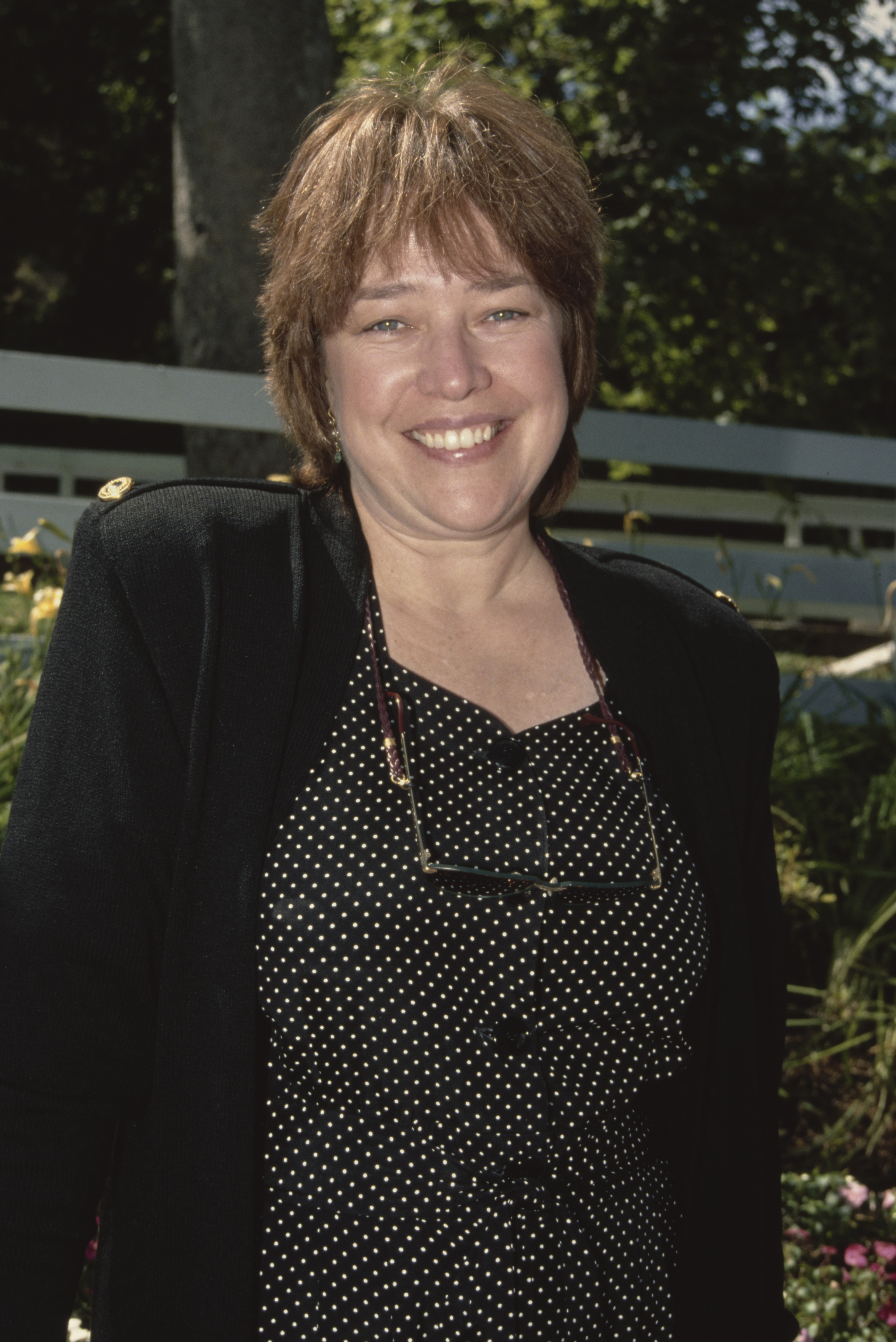 Kathy Bates, wearing a a black jacket over a black outfit with white polka dots, a pair of glasses hanging from a cord around her neck, in 1993. | Source: Getty Images