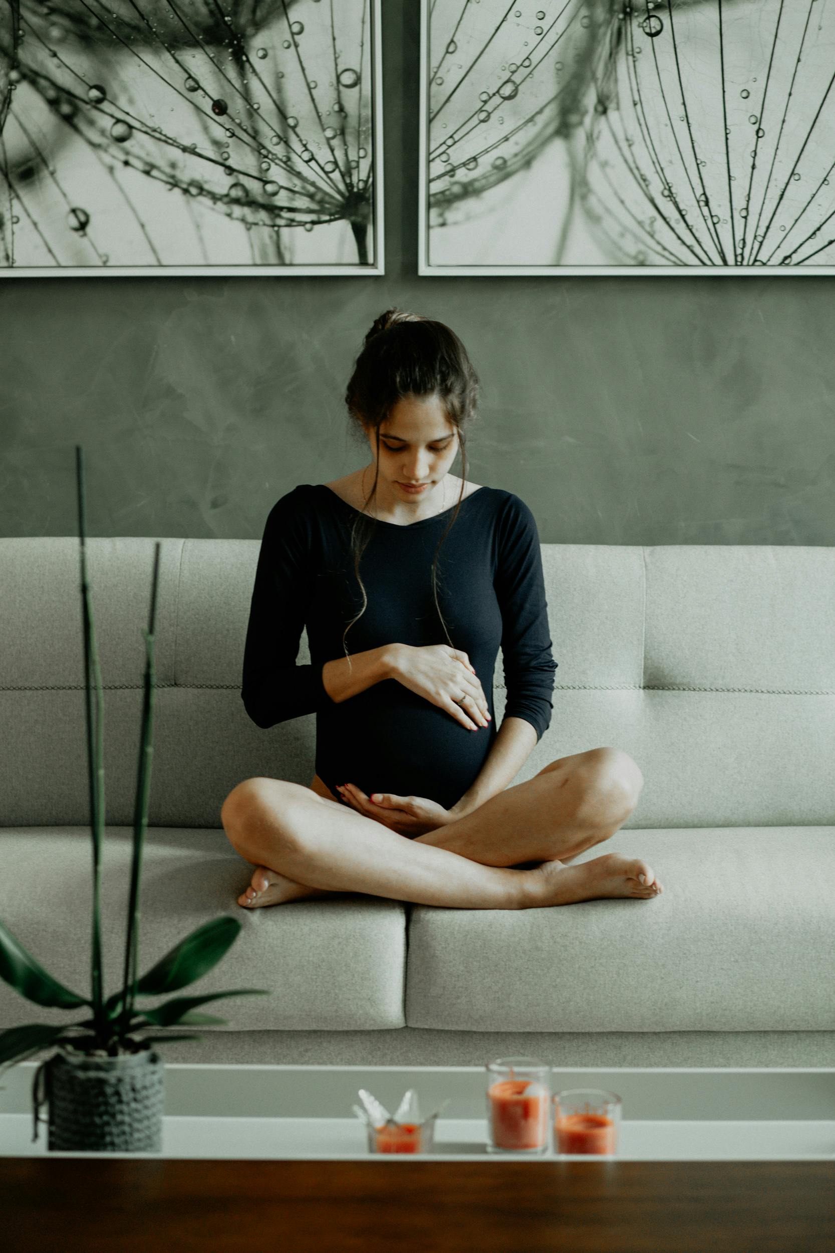 A pregnant woman sitting on the couch while touching her belly | Source: Pexels