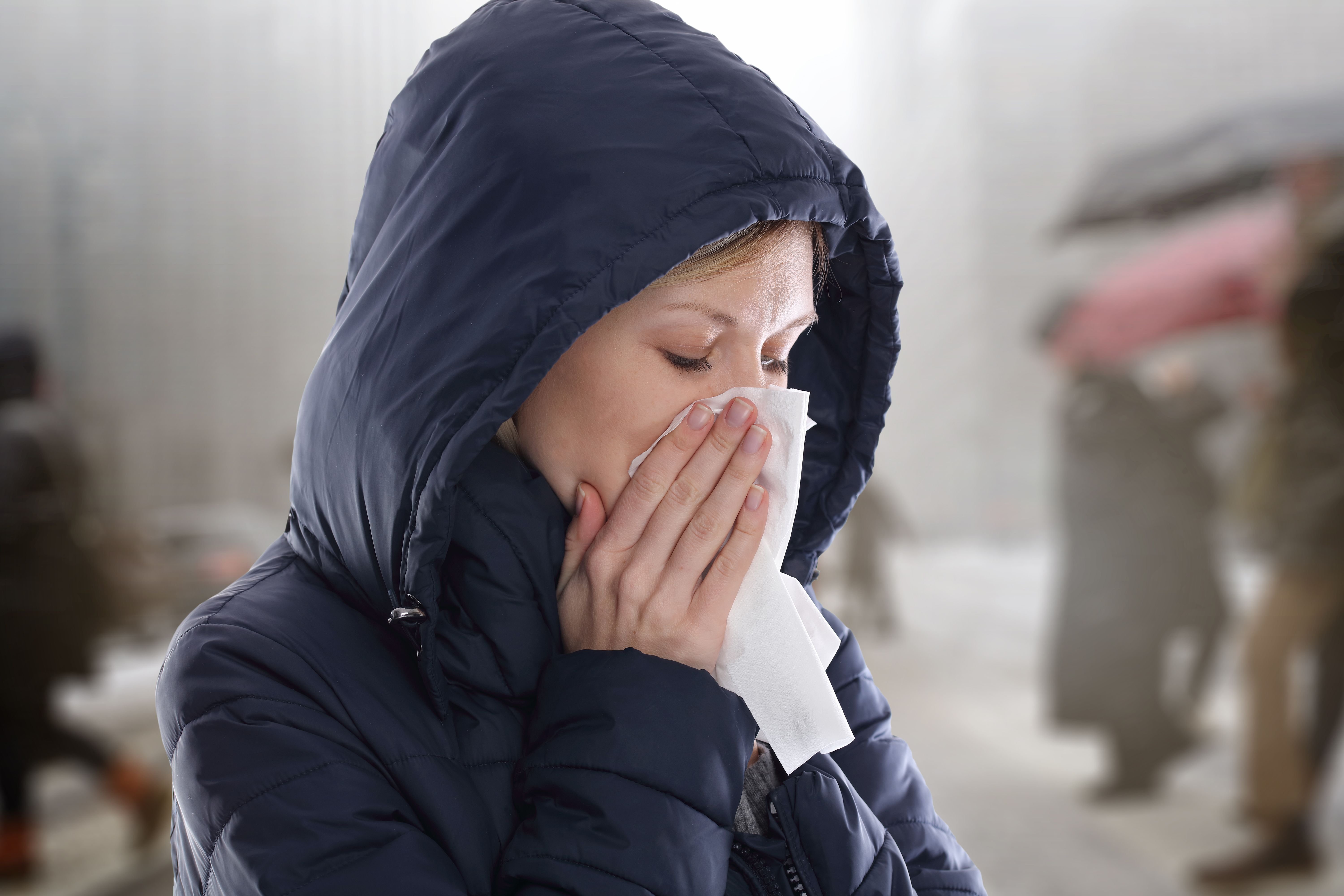 A sick woman blows her nose on tissue. | Source: Shutterstock