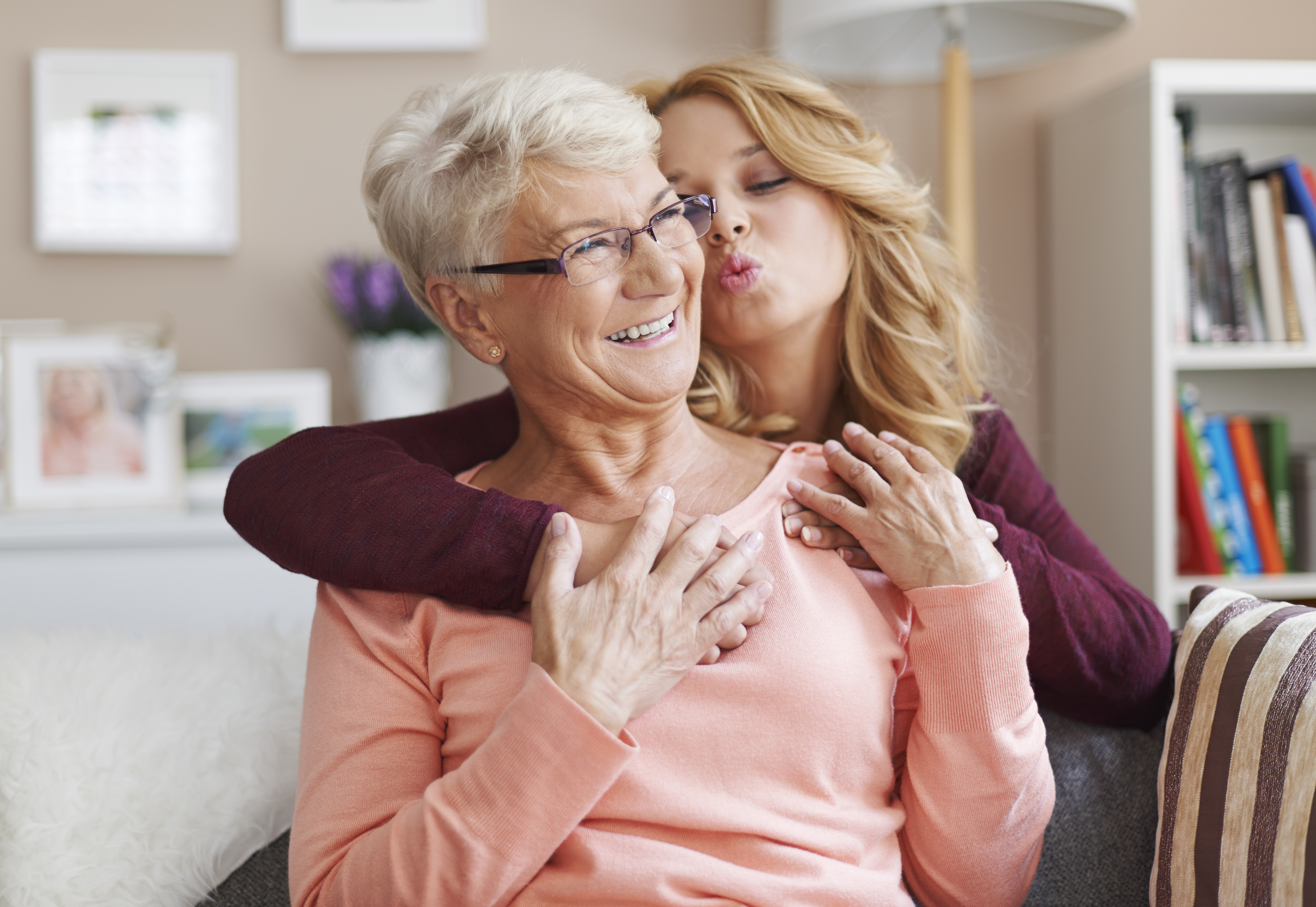 Teen girl hugging her smiling grandmother from behind and attempting to kiss her | Source: gpointstudio on Freepik