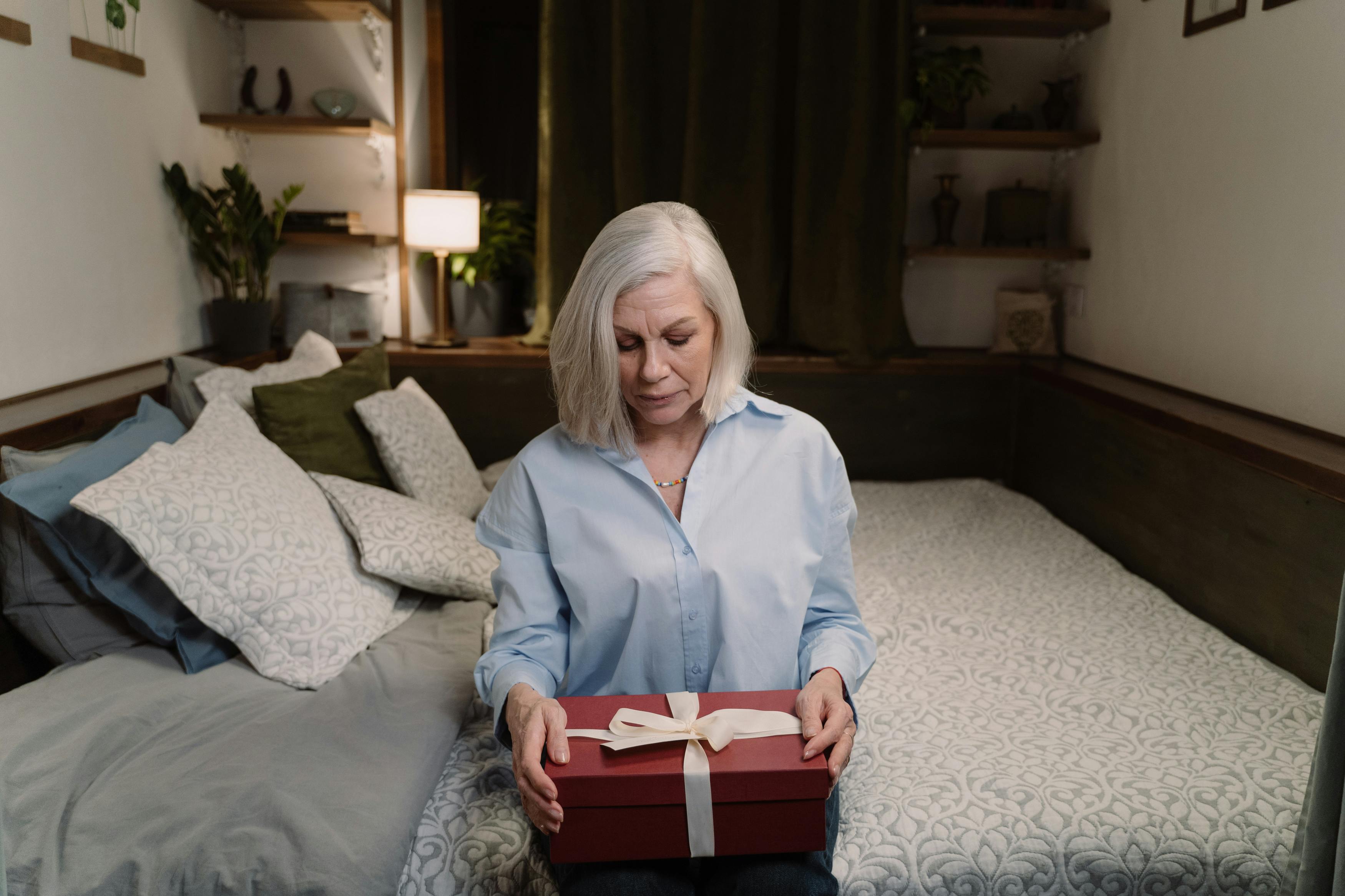 A woman holding a box while seated on a bed | Source: Pexels