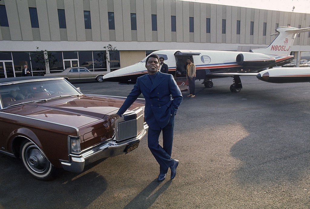 James Brown leans on the hood of a 1970 Lincoln Continental Mark III Coupe car parked in front of a Learjet 24A airplane at Los Angeles International Airport, 1969. | Photo: Getty Images