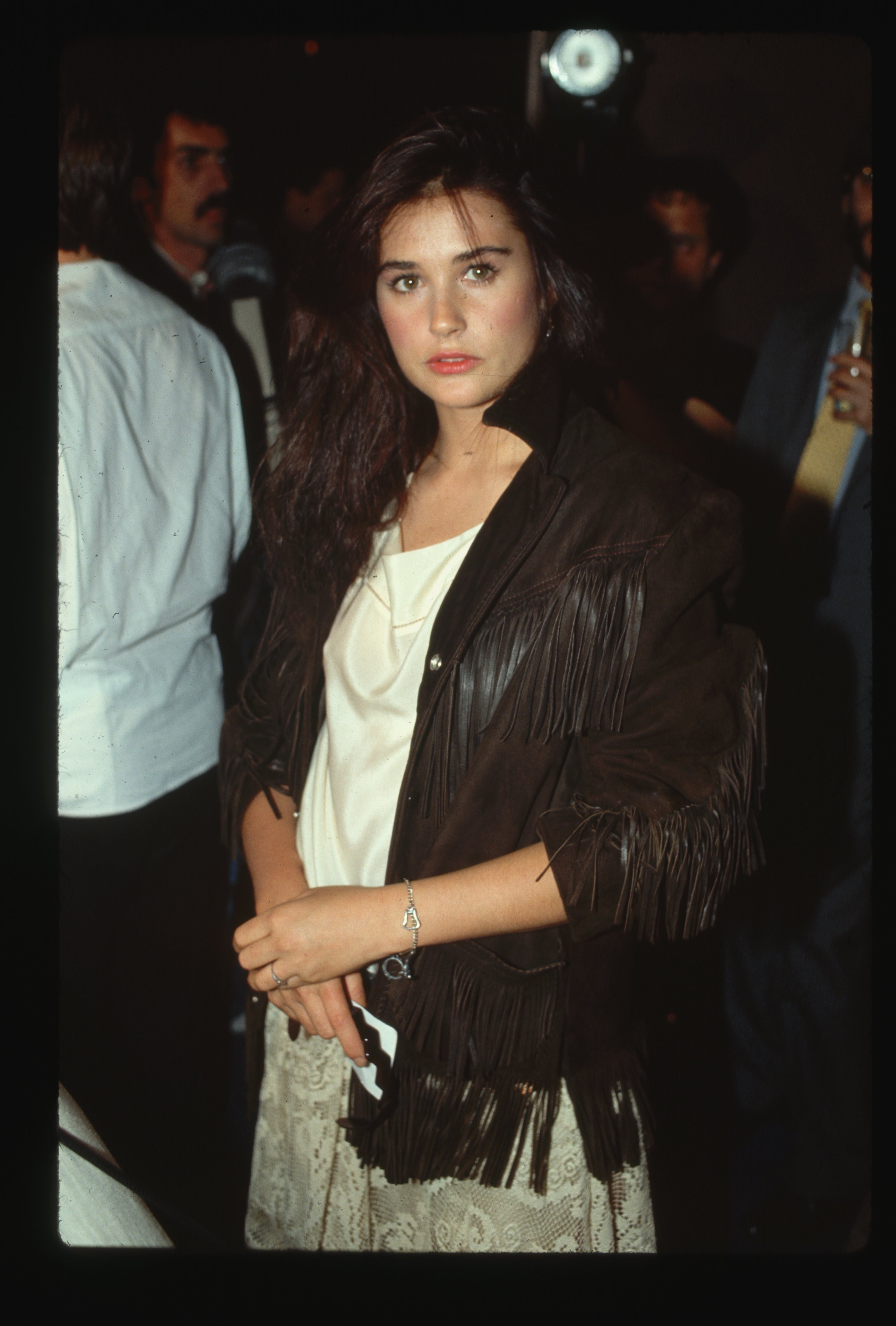 Demi Moore pictured wearing a black fringed, leather coat with a beige outfit in 1985. / Source: Getty Images