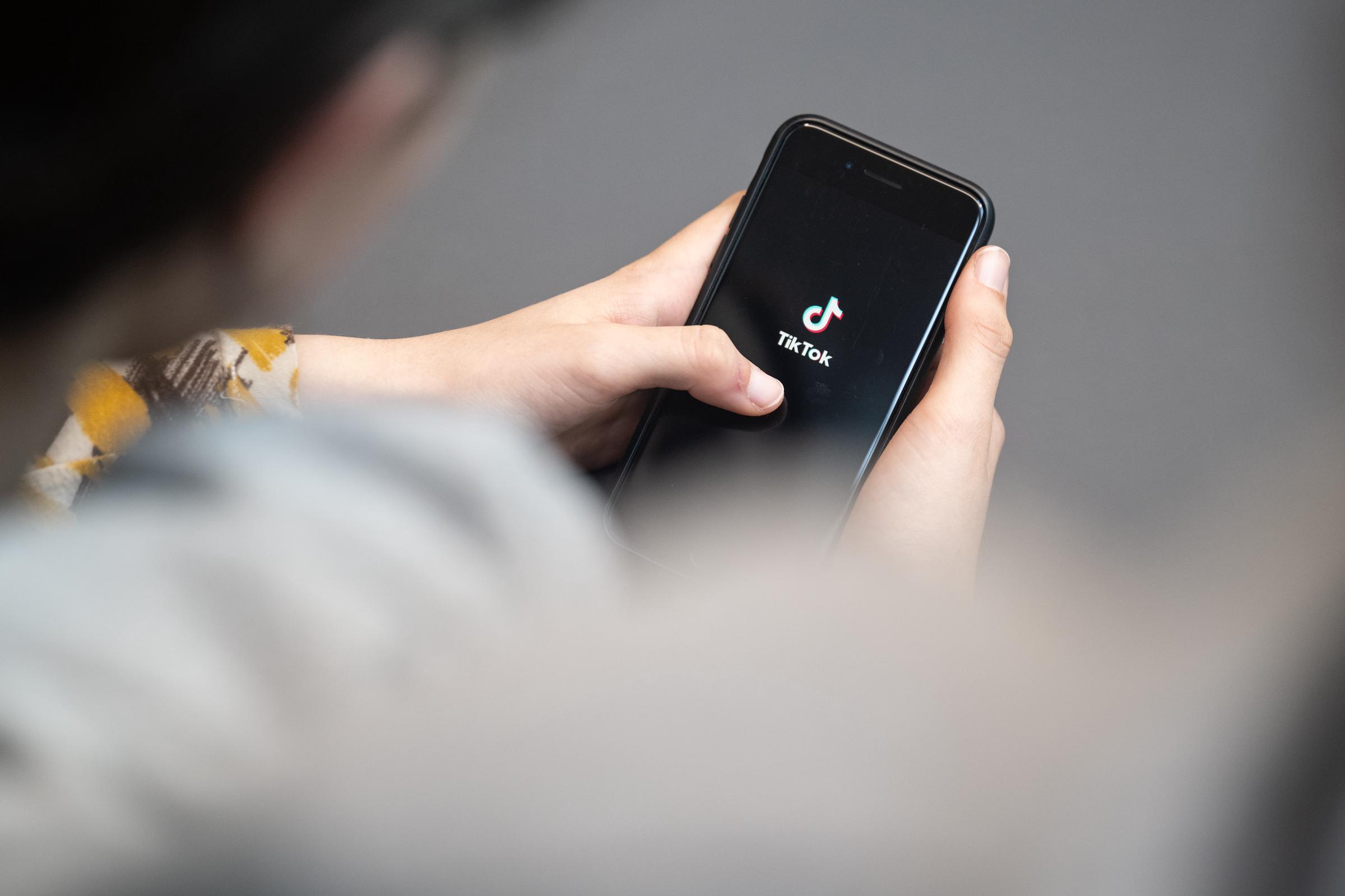 A teenager looks at a smartphone with the TikTok logo | Source: Getty Images