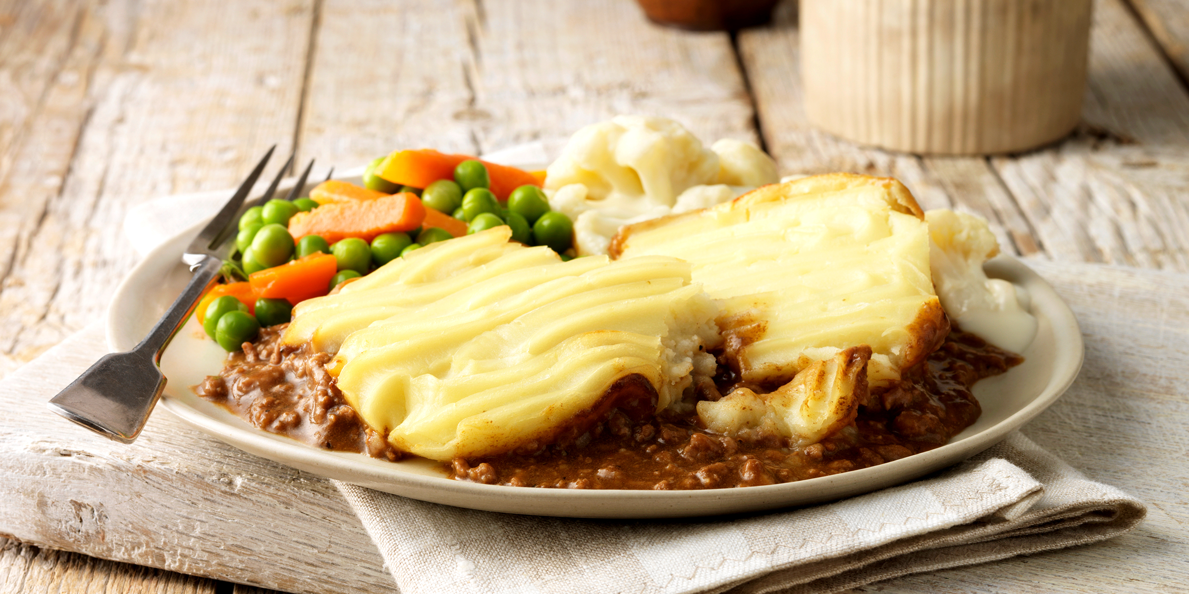 A plate of shepherd's pie paired with peas, carrots, and cauliflower | Source: Getty Images