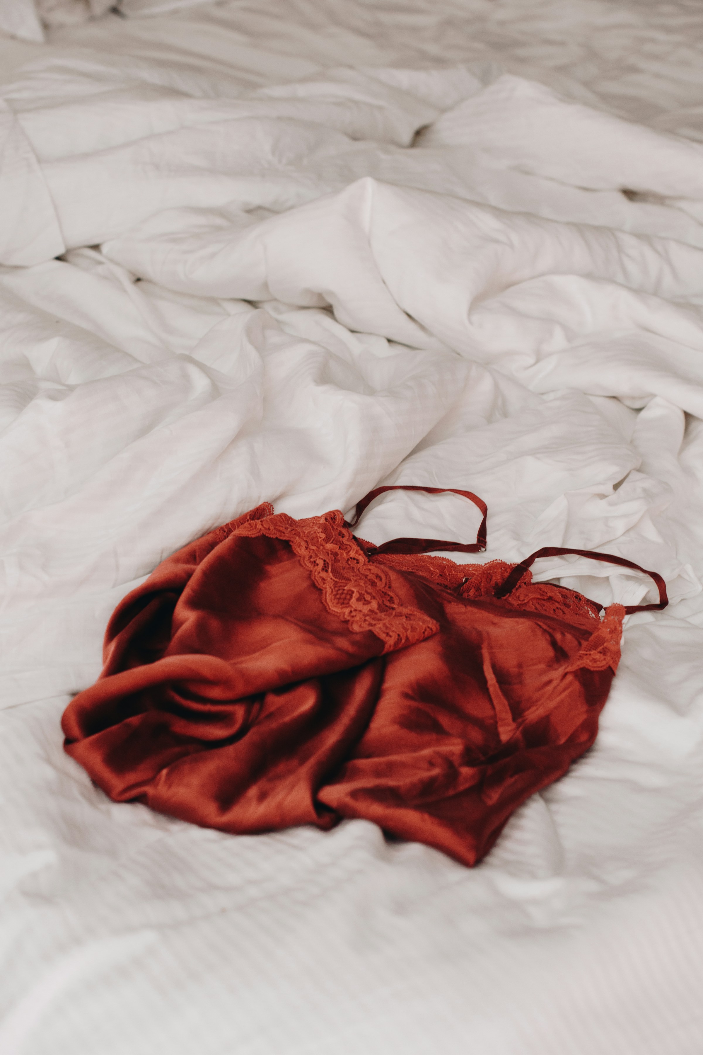 Red laced lingerie lying on white linen sheets | Source: Unsplash