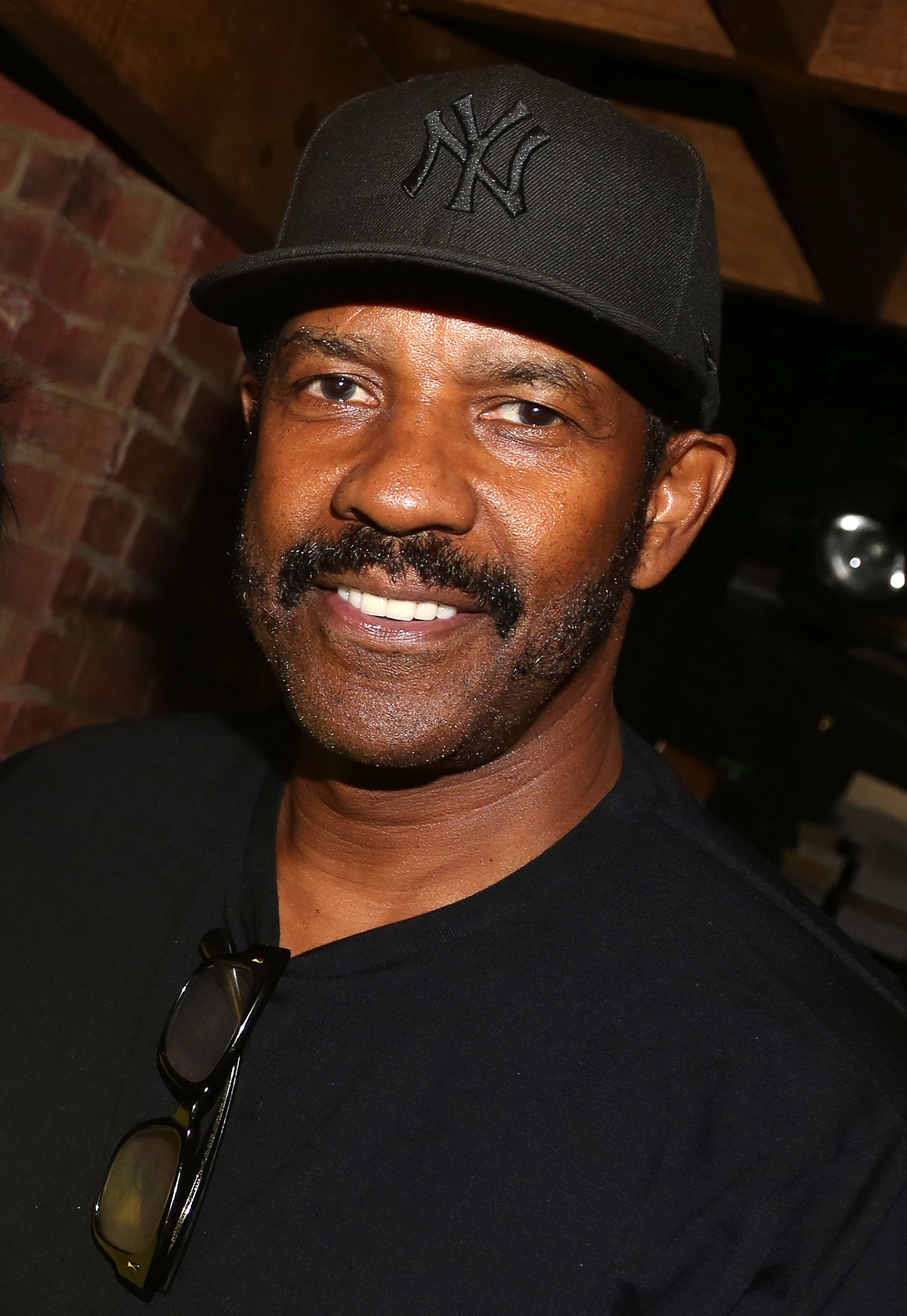 Backstage at "Hamilton," Denzel Washington sports a casual look with a curved brim Yankees cap. His mustache and rugged and slight beard stand out beneath the cap, giving off an effortlessly cool, off-duty vibe.