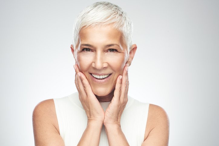Belle femme âgée souriante aux cheveux gris courts posant devant un fond gris. | Photo : Getty Images
