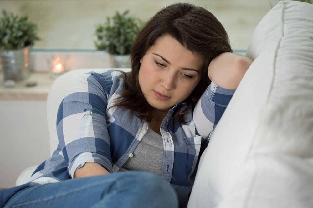 A photo of a young concerned woman sitting on a couch. | Photo: Shutterstock