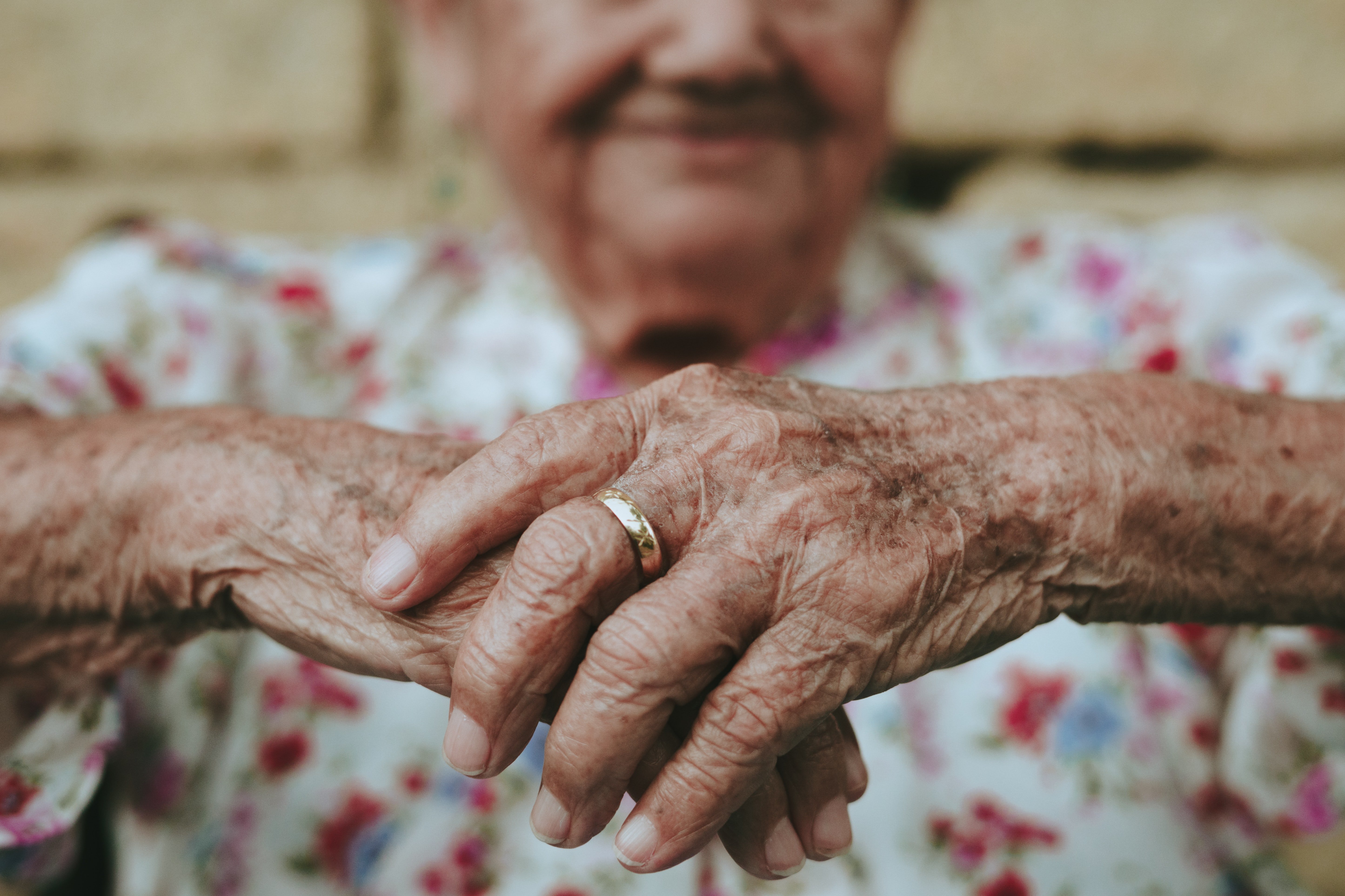 Una anciana sosteniendo sus manos recostada de un muro. | Foto: Unsplash