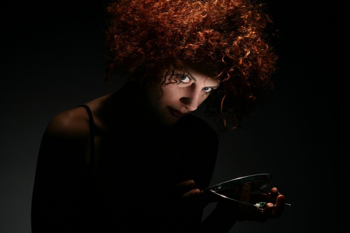 Mujer en la oscuridad con mirada intensa y espejo de mano. | Imagen: PxHere
