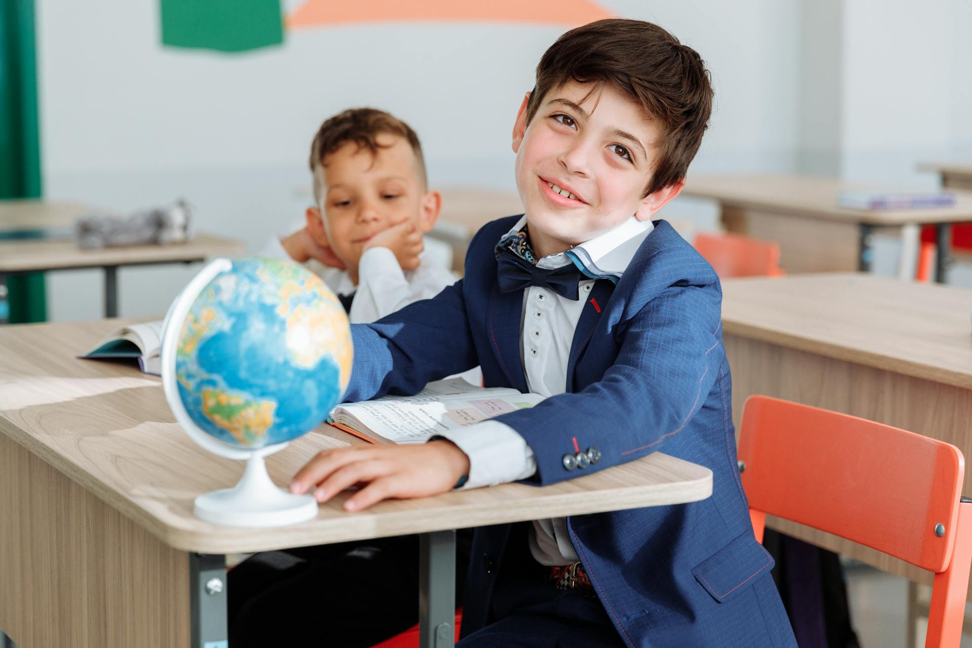 A young boy sitting in the classroom with his friend and smiling | Source: Pexels