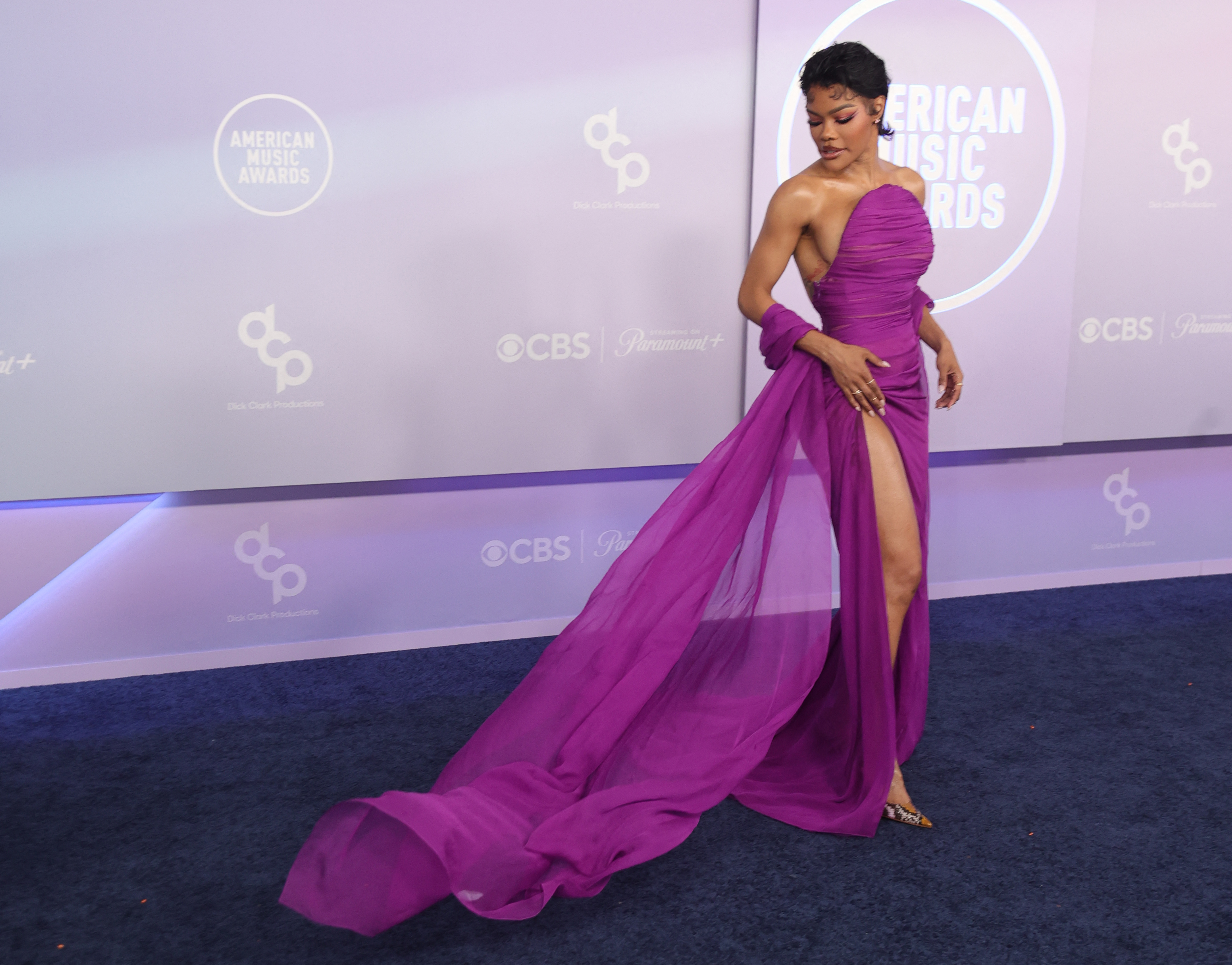 eyana Taylor looks down at the flowing train of her purple gown as it stretches across the blue carpet behind her | Source: Getty Images