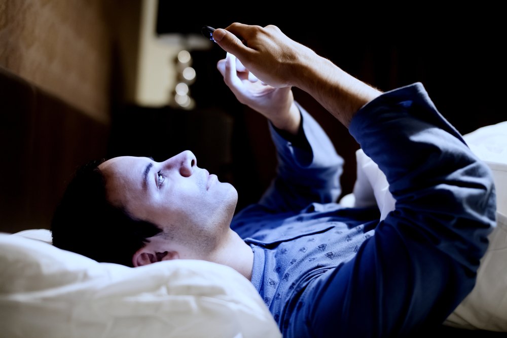 Un homme utilisant son téléphone portable au lit avant de s'endormir. | Shutterstock