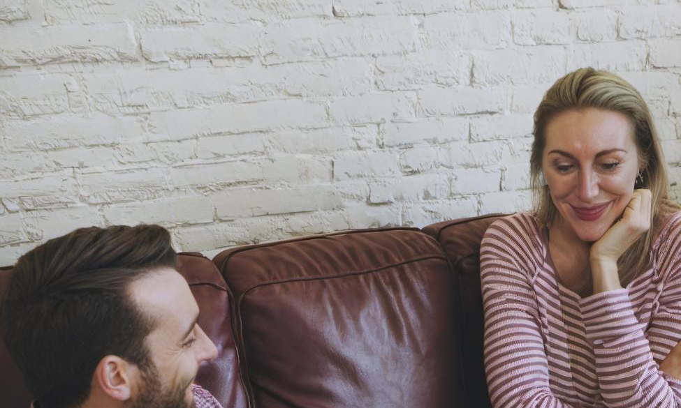 A man and woman having a friendly conversation on a sofa | Source: Midjourney