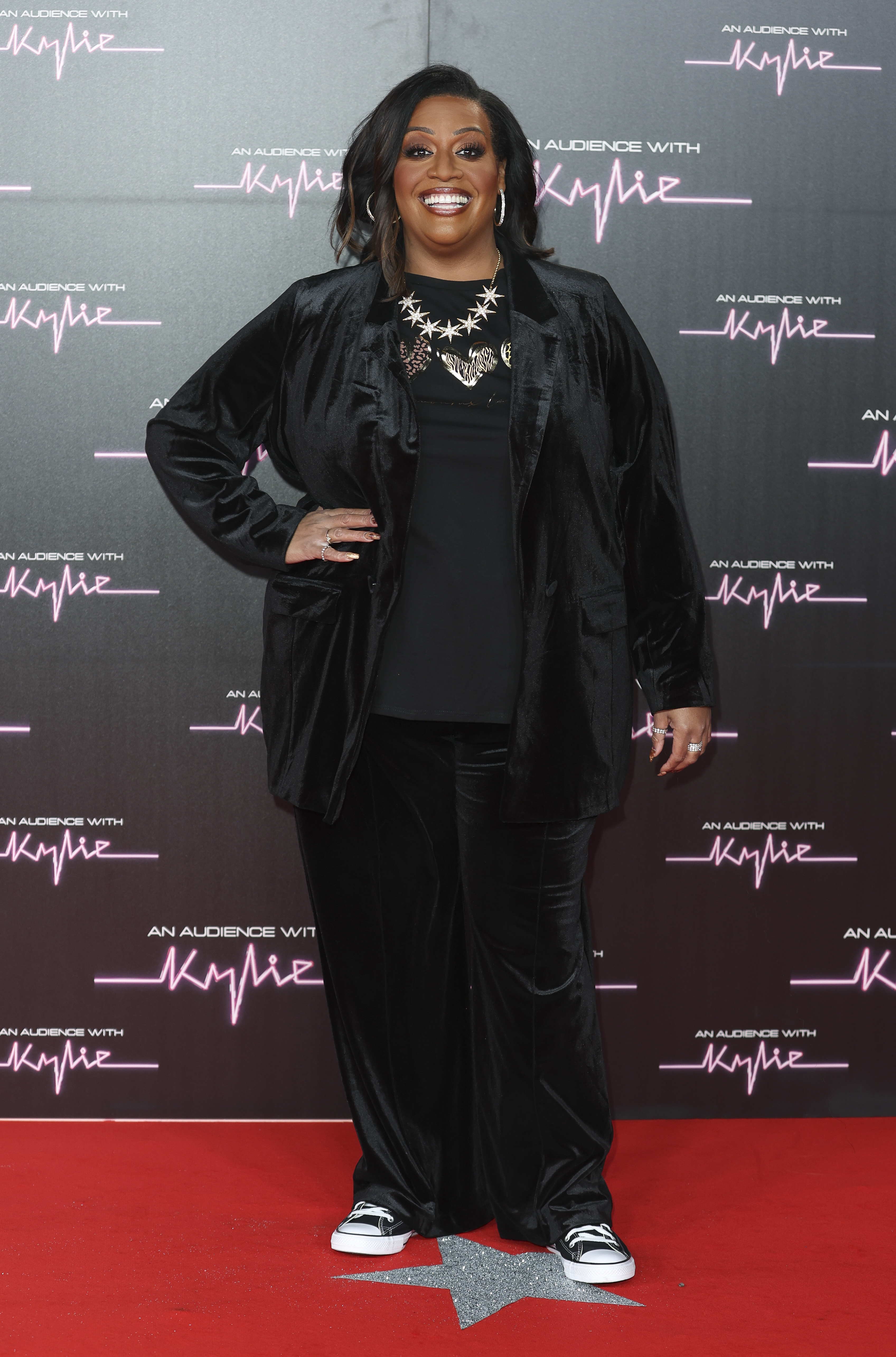 Looking sleek and stylish, Hammond hits the red carpet at the Royal Albert Hall for "An Audience With Kylie" on 1 December 2023. Her all-black ensemble — velvet trousers, trainers and a sharp jacket — is finished with a bold star necklace and hoops against a neon-inspired backdrop.