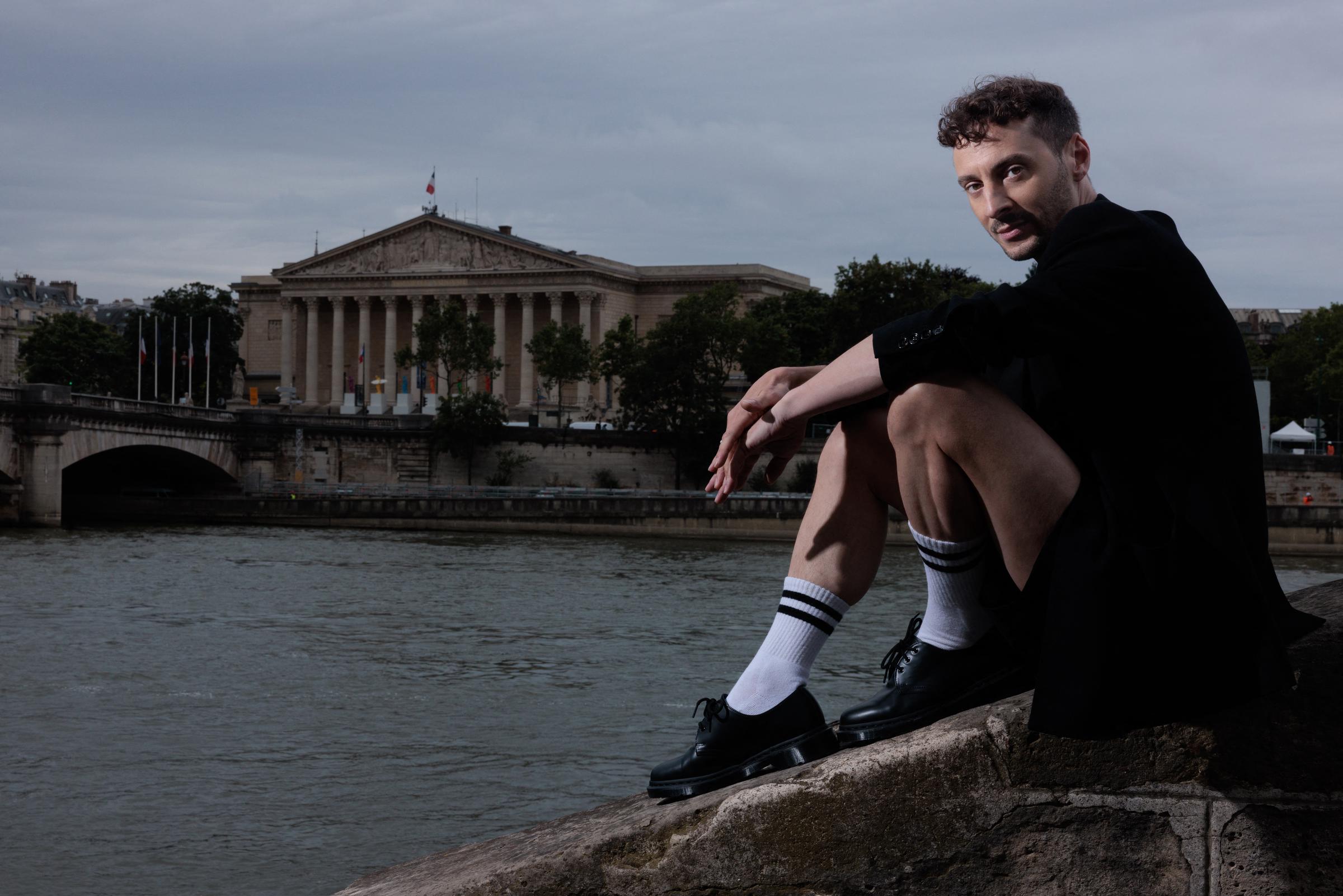 Thomas Jolly, poses sitting on a wall near the Seine River with the Eiffel tower in the background, in Paris, France, on July 2, 2024. | Source: Getty Images