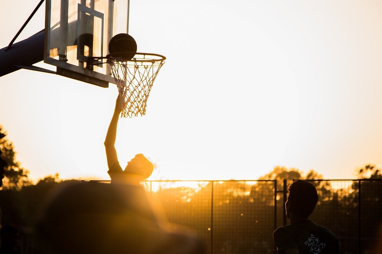 A sunset silhouette of a basketball player dunking a ball in the net | Photo: Pixabay/Varun Kulkarni