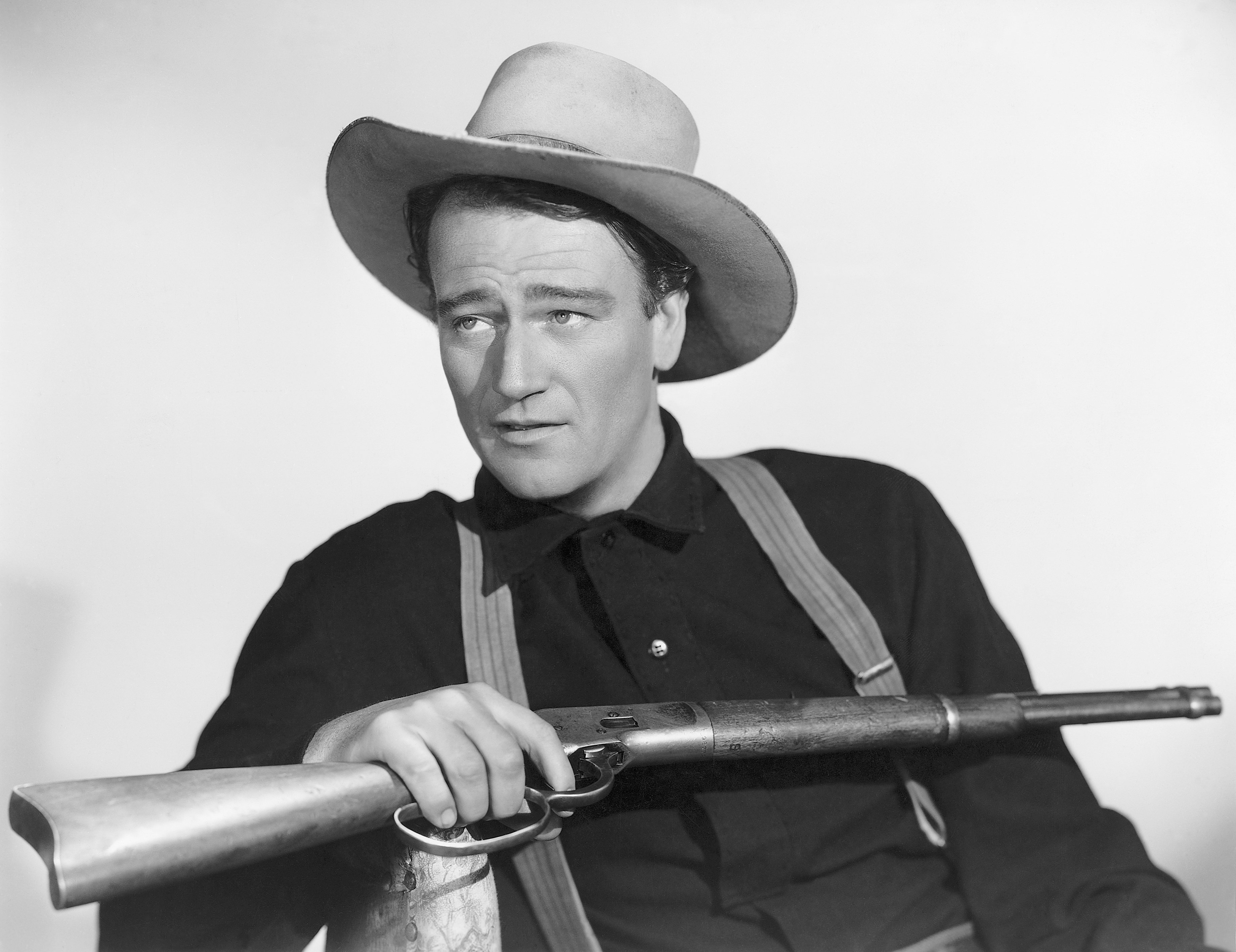 John Wayne holding a rifle in a publicity photo for the movie Shepherd of the Hills.| Source: Getty Images