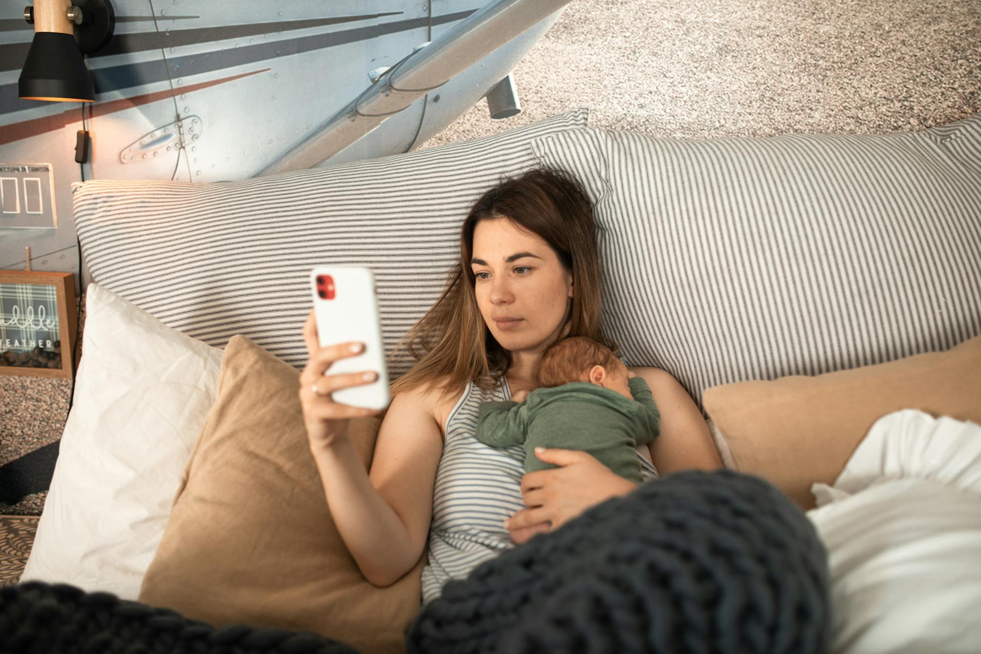 A woman lying down and using her phone with her baby sleeping on her chest | Source: Pexels