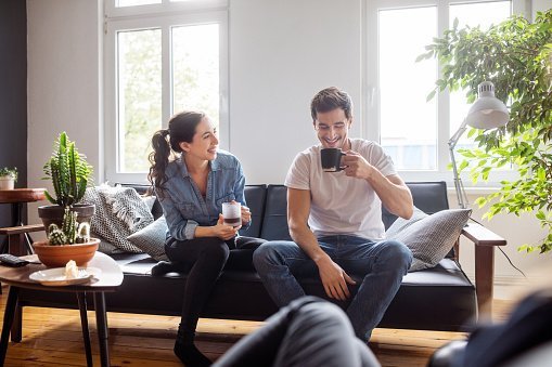 Cheerful young man and woman sitting on sofa | Photo: Getty Images