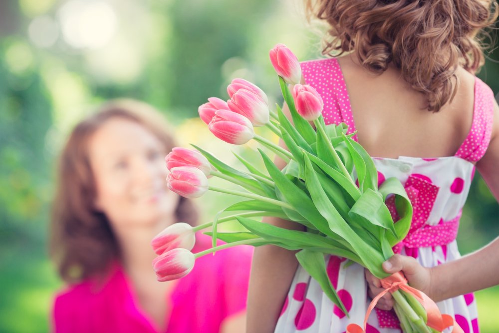 Frau und Kind mit Blumenstrauß auf grünem, unscharfem Hintergrund. I Quelle: Shutterstock