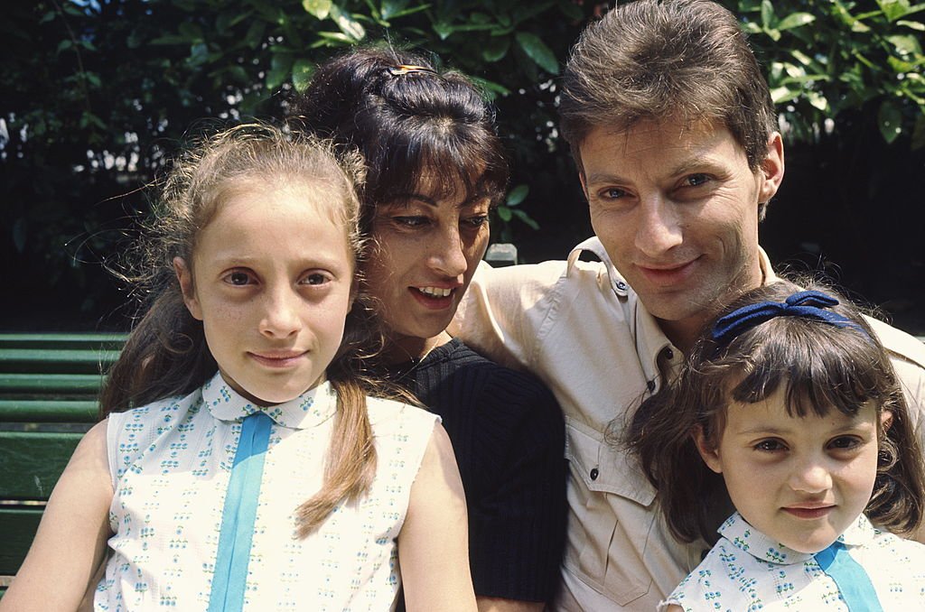  Hugues Aufray et sa femme Hélène assis sur un banc, avec leurs deux filles Charlotte et Marie | photo : Getty Images